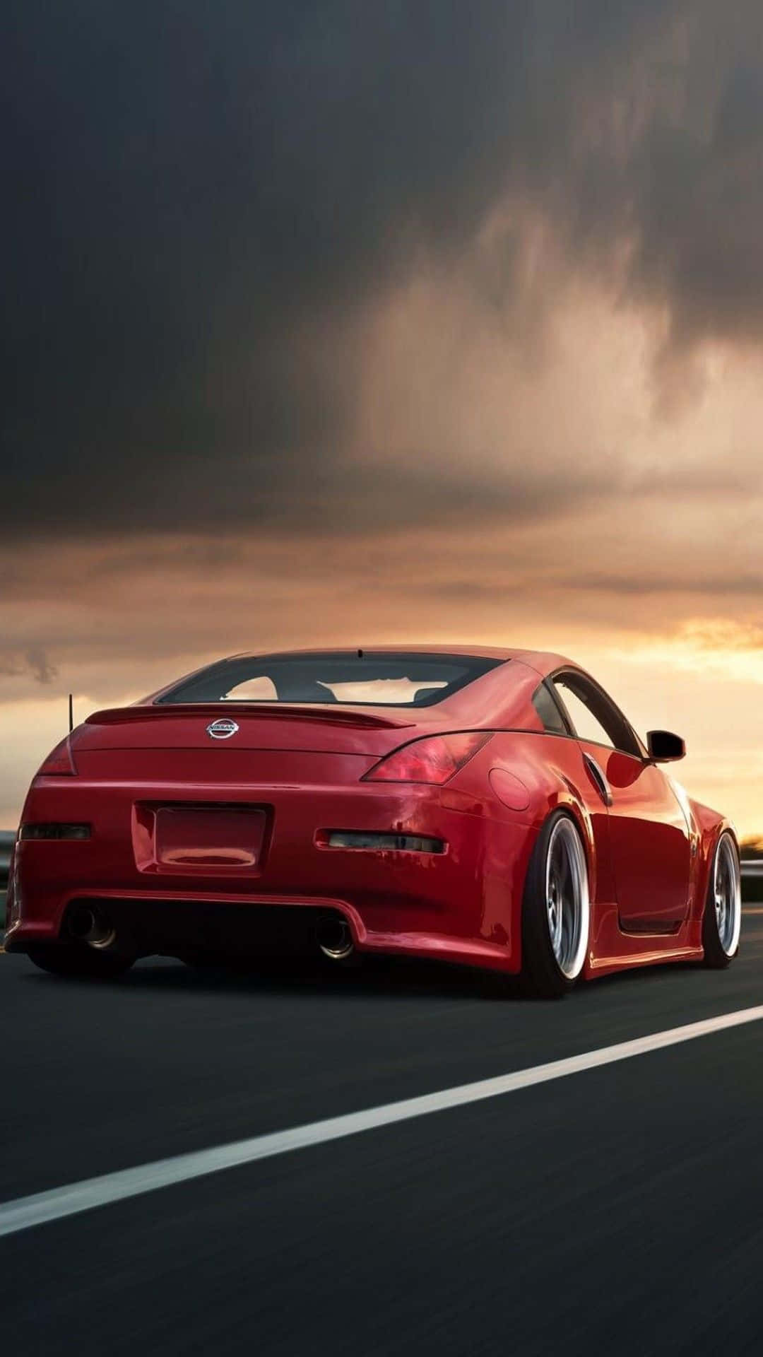 駕駛Nissan 350Z，穿梭城市 壁紙 — 一輛亮麗的紅色跑車在高速公路上行駛，天空是戲劇性的日落，烏雲密佈。