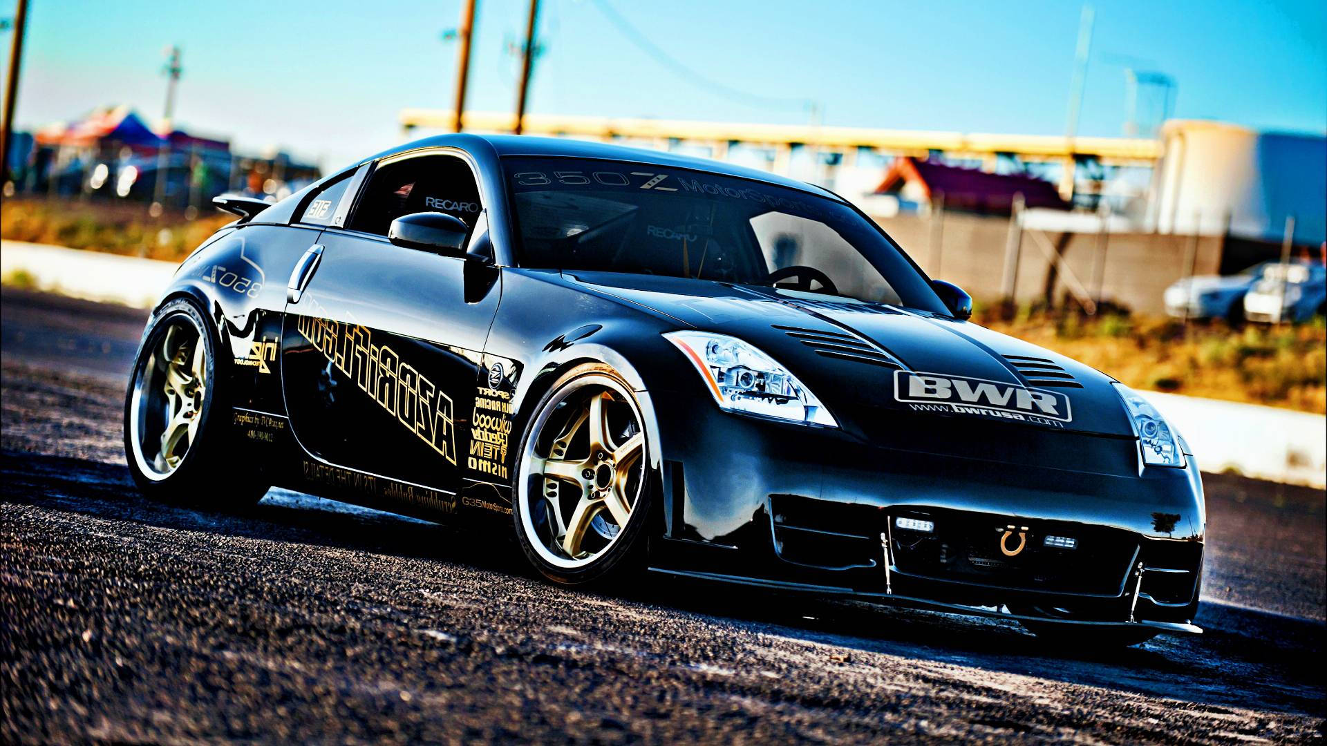 Nissan 350Z：經典且樂趣十足的跑車 壁紙 — 一架時尚黑色飄移車，配金色輪圈及贊助商貼紙，在陽光普照的瀝青賽道上奔馳。
