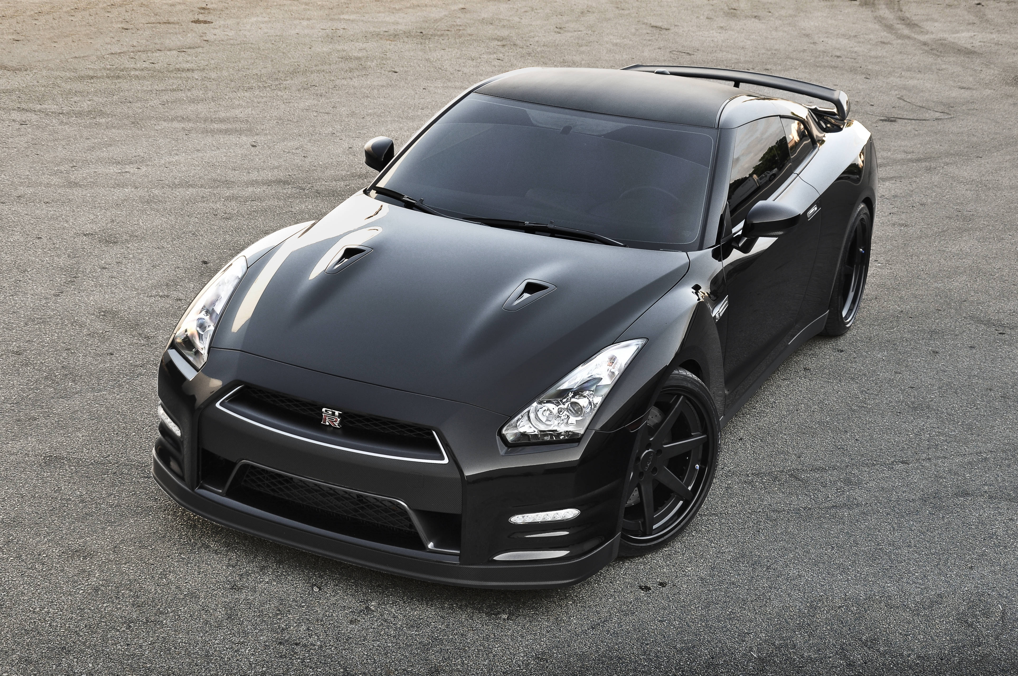 Nissan GT-R 深黑車色 壁紙 — 一輛時尚的啞光黑色日產GT-R跑車停在灰色瀝青路面上，在明亮的日光下。