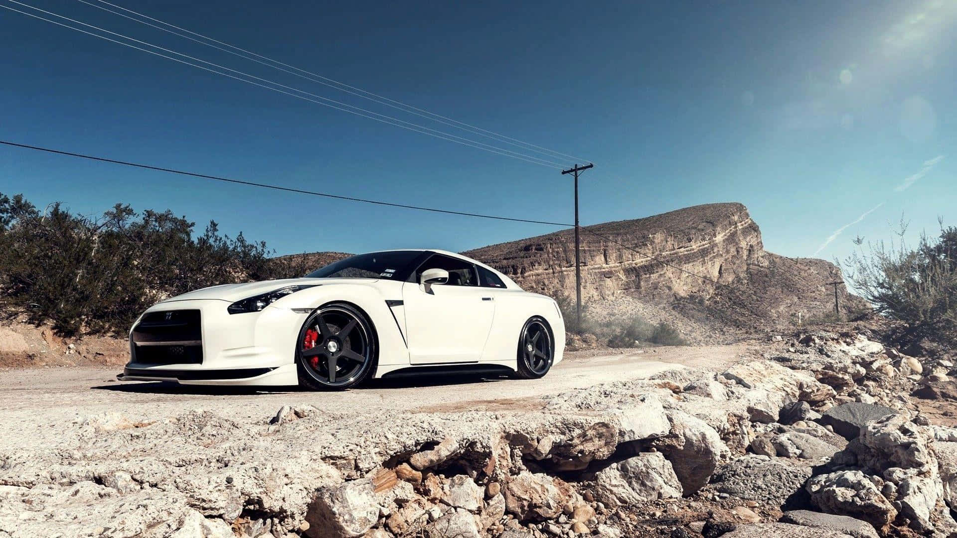Nissan GTR：動力與奢華的完美結合 壁紙 — 一架純白色日產GT-R跑車停泊在岩石沙漠道路上，背景是晴朗藍天和崎嶇懸崖。