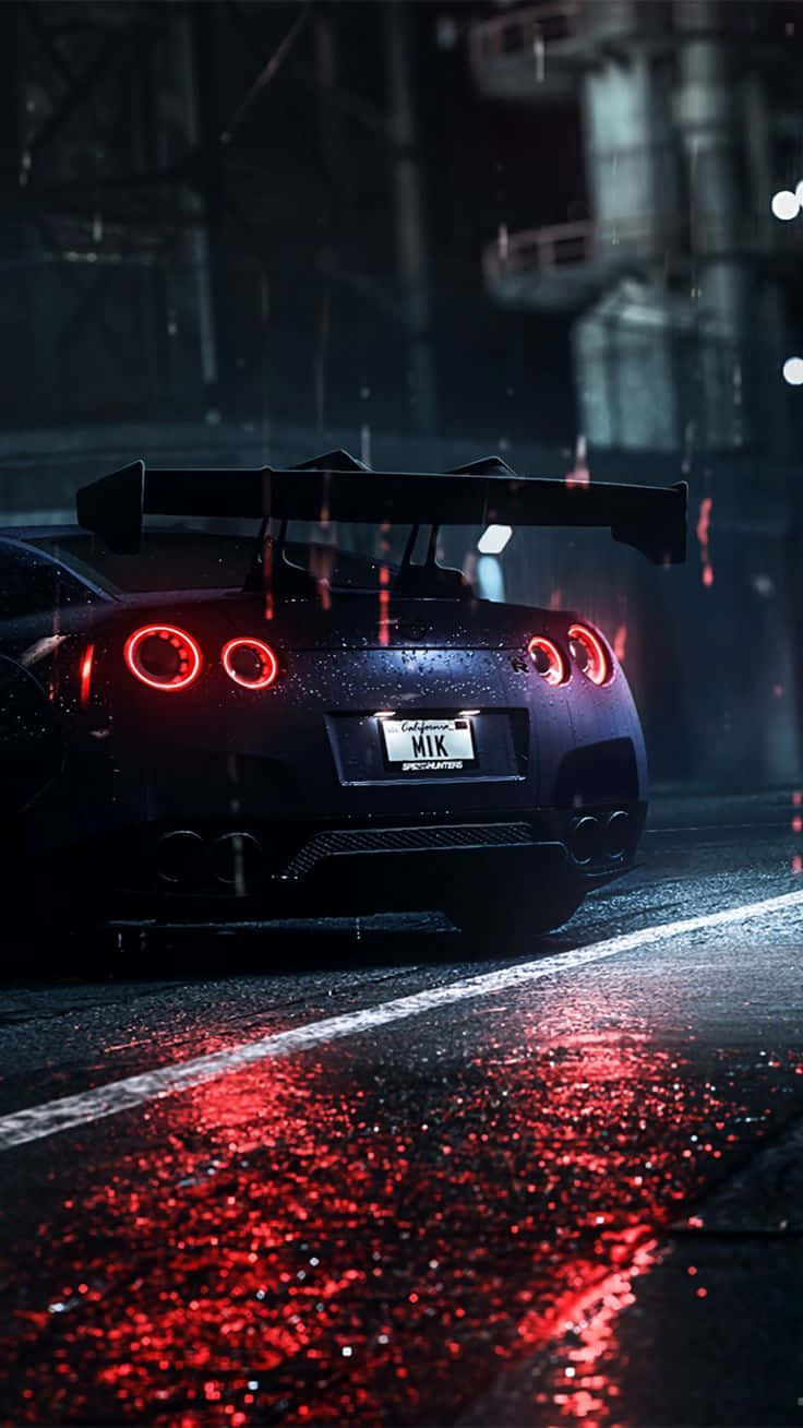 Nissan R35 GT-R 尾燈圖 壁紙 — 一輛黑色跑車帶有發光的紅色尾燈，在夜晚的雨中行駛在濕漉漉的城市街道上。