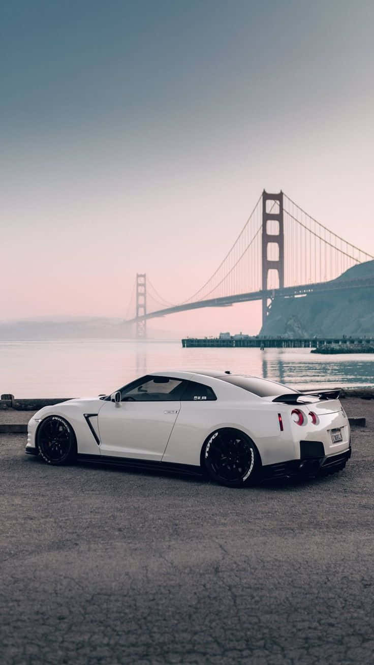 Nissan R35 GT-R橋樑背景圖 壁紙 — 一架時尚的白色跑車停在海濱，金門大橋在柔和的粉紅色和藍色暮色薄霧中閃耀。