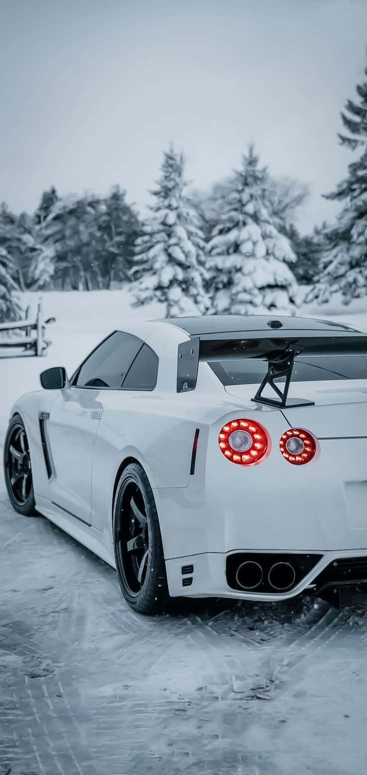 Nissan R35 GT-R雪地手機壁紙圖 壁紙 — 一輛白色跑車帶有發光的紅色尾燈，停在雪地上，周圍是白雪覆蓋的松樹。