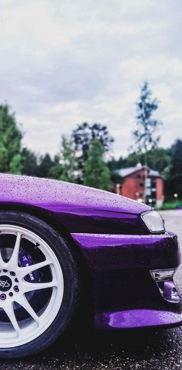 紫色跑車表面有雨滴，停在樹木附近。
