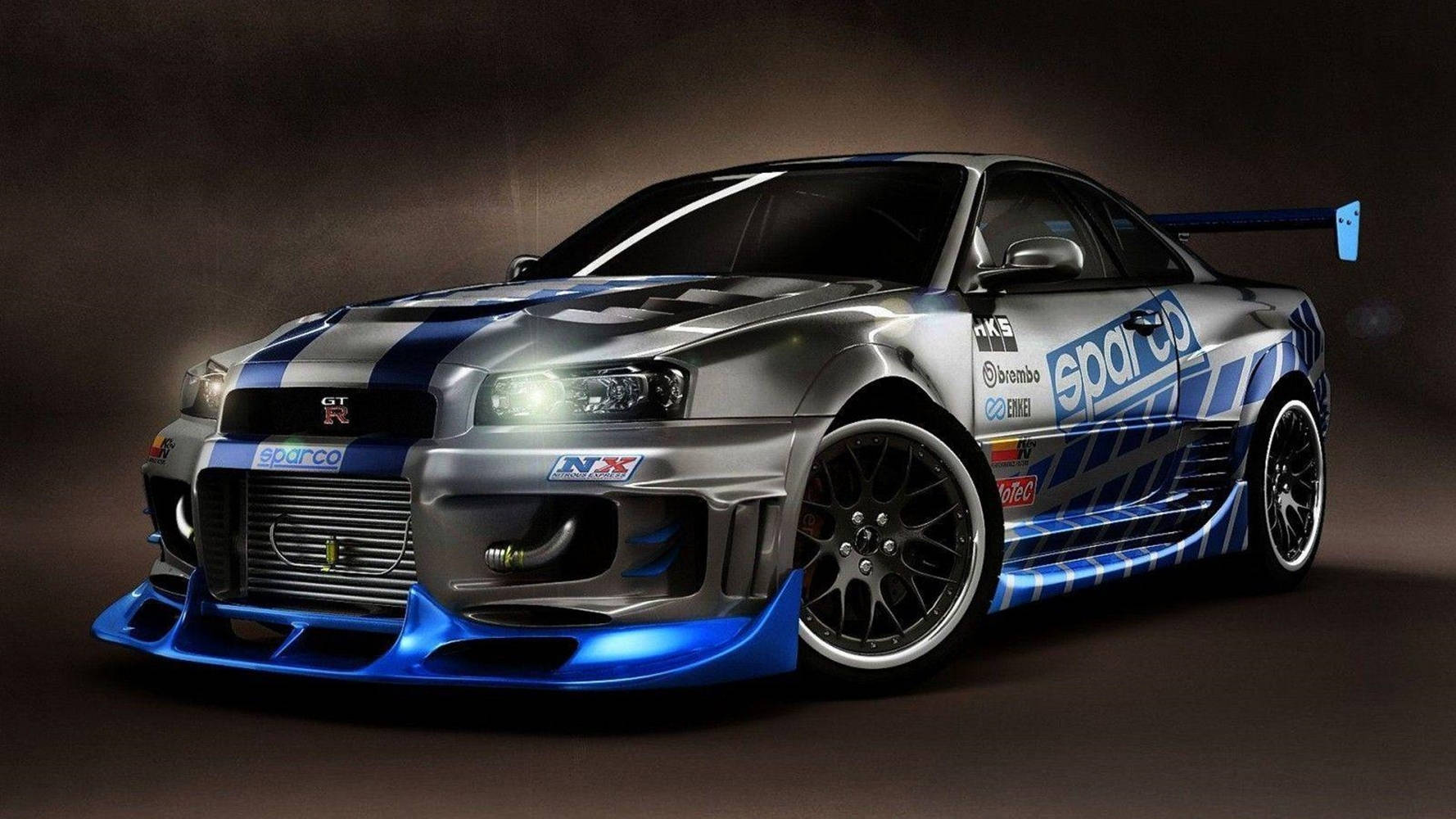 Nissan Skyline 行動瞬間 - 快速與狂野系列經典車款 壁紙 — 一架時尚的銀藍色賽車，帶有贊助商貼紙和發光頭燈，在黑暗的攝影棚中戲劇性地擺姿勢。