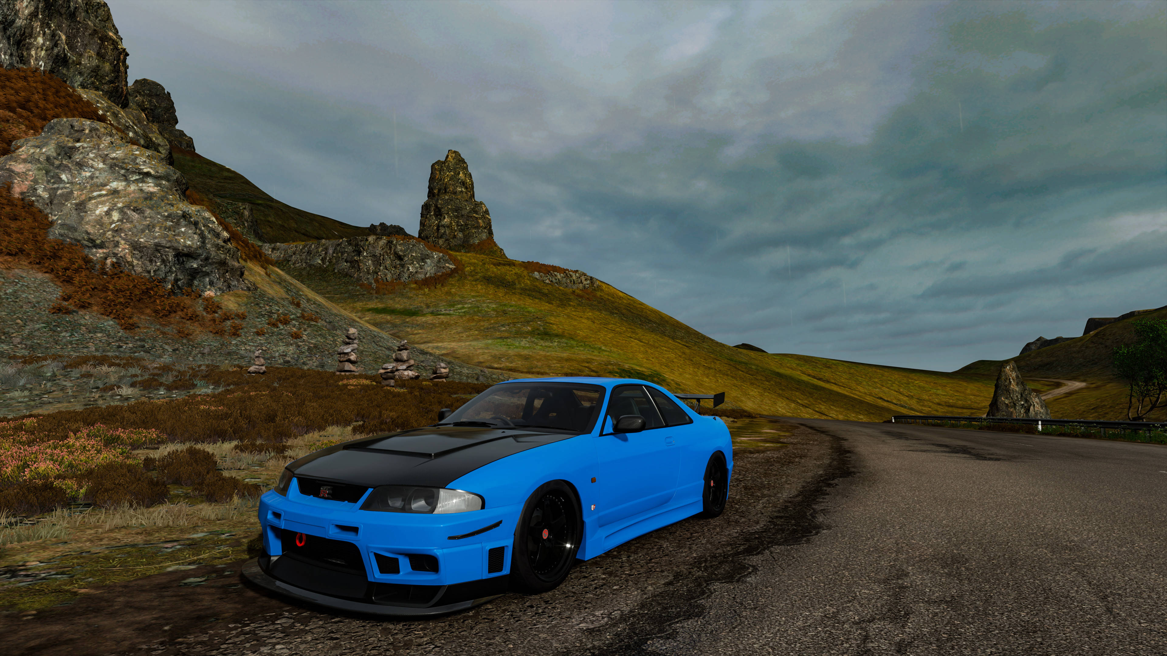 Nissan Skyline GTR R33 冰島公路 壁紙 — 一輛帶有黑色裝飾的充滿活力的藍色跑車停泊在蜿蜒的山路上，天空陰沉多雲。