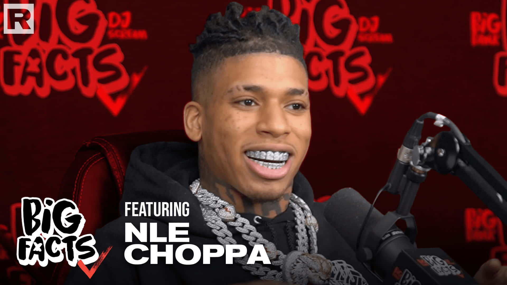NLE Choppa 桌布 壁紙 — NLE Choppa 戴住 grillz 坐喺紅色 'Big Facts' 品牌背景前，露出燦爛笑容。