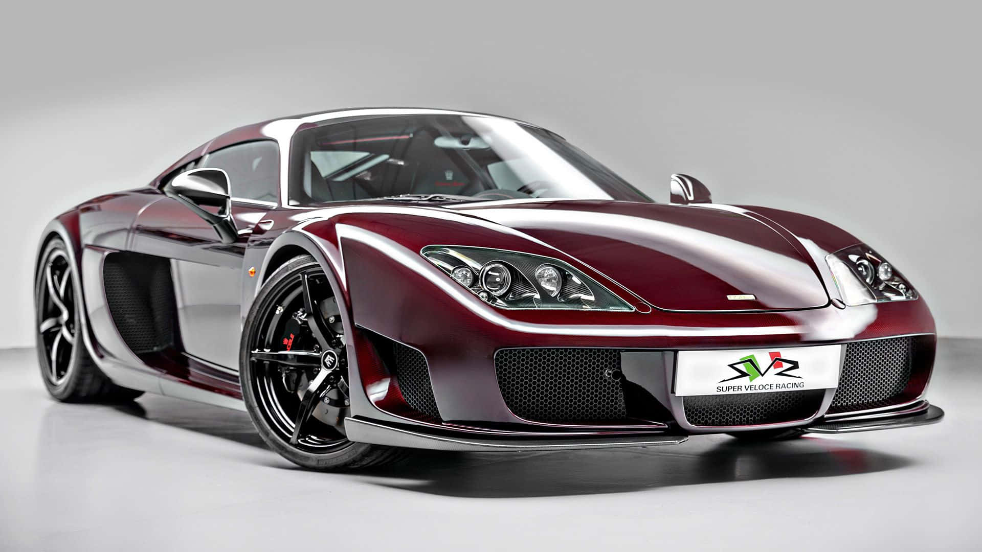 Noble M600 前臉 壁紙 — 一輛時尚的栗色和銀色超級跑車，配備黑色車輪，在簡約的攝影棚環境中擺拍。