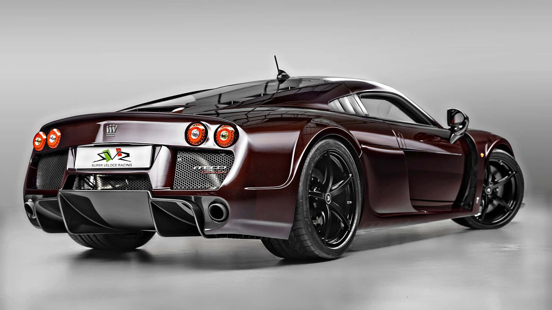 朱紅色Noble M600 壁紙 — 一輛光澤的栗色超級跑車，帶有黑色飾件和橙色尾燈，從後方四分之三角度展示在灰色工作室背景前。