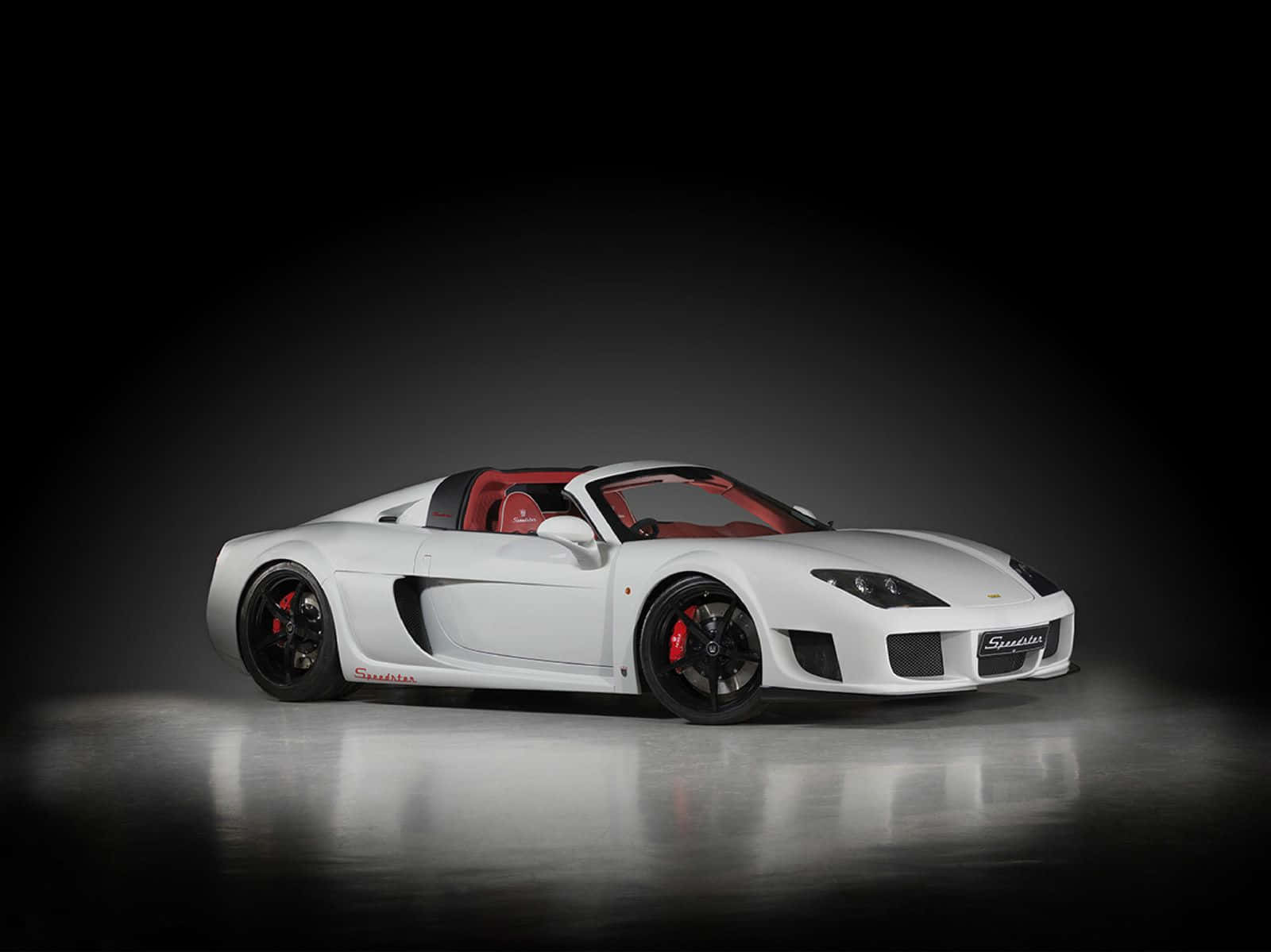 展廳中的尊貴白色Noble車款 壁紙 — 一架時尚的白色Spyder跑車，配備紅色內飾和黑色輪圈，在帶有反射地板的深色工作室背景下展示。