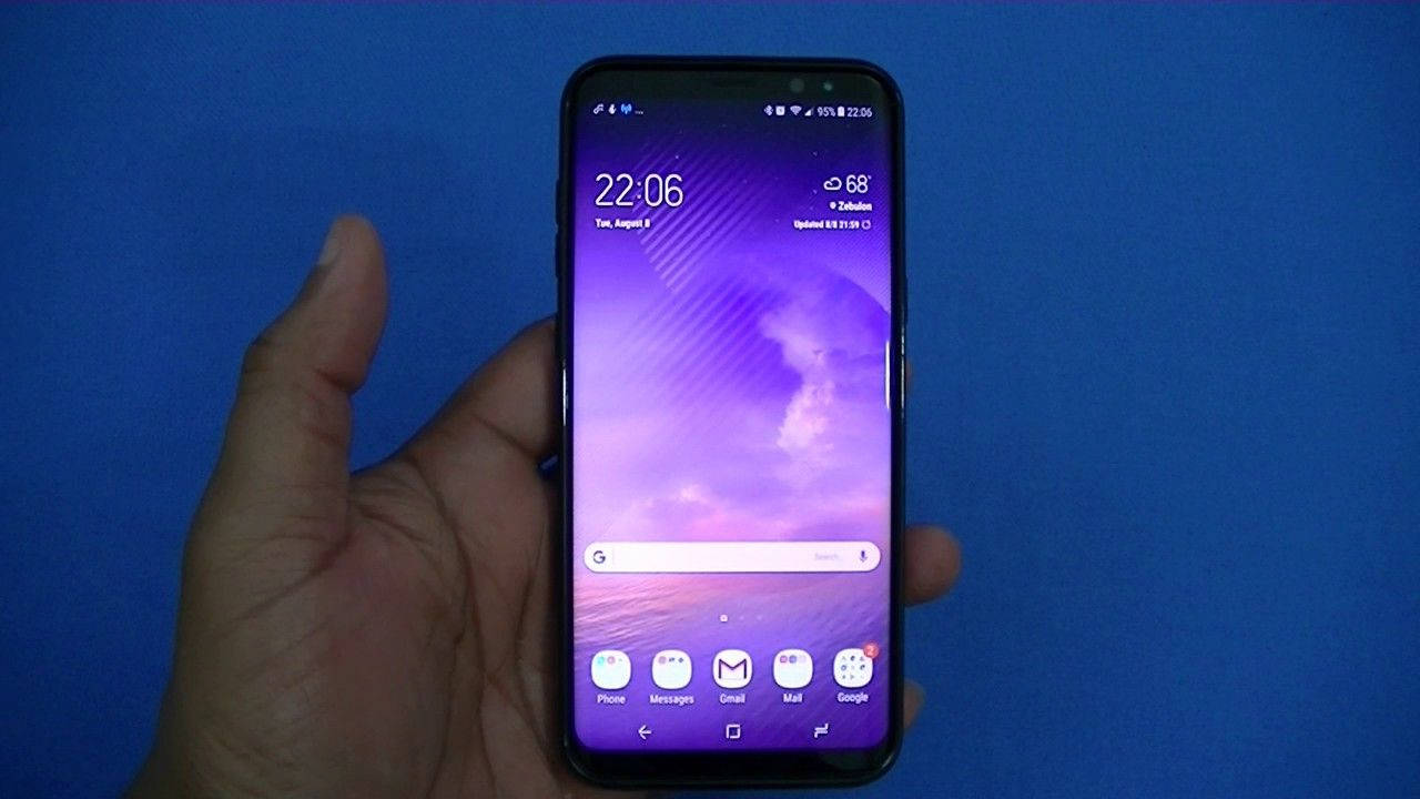 手持 Note 8 手機 壁紙 — 一隻手拿著智能手機，在純藍色背景上顯示紫色日落壁紙。