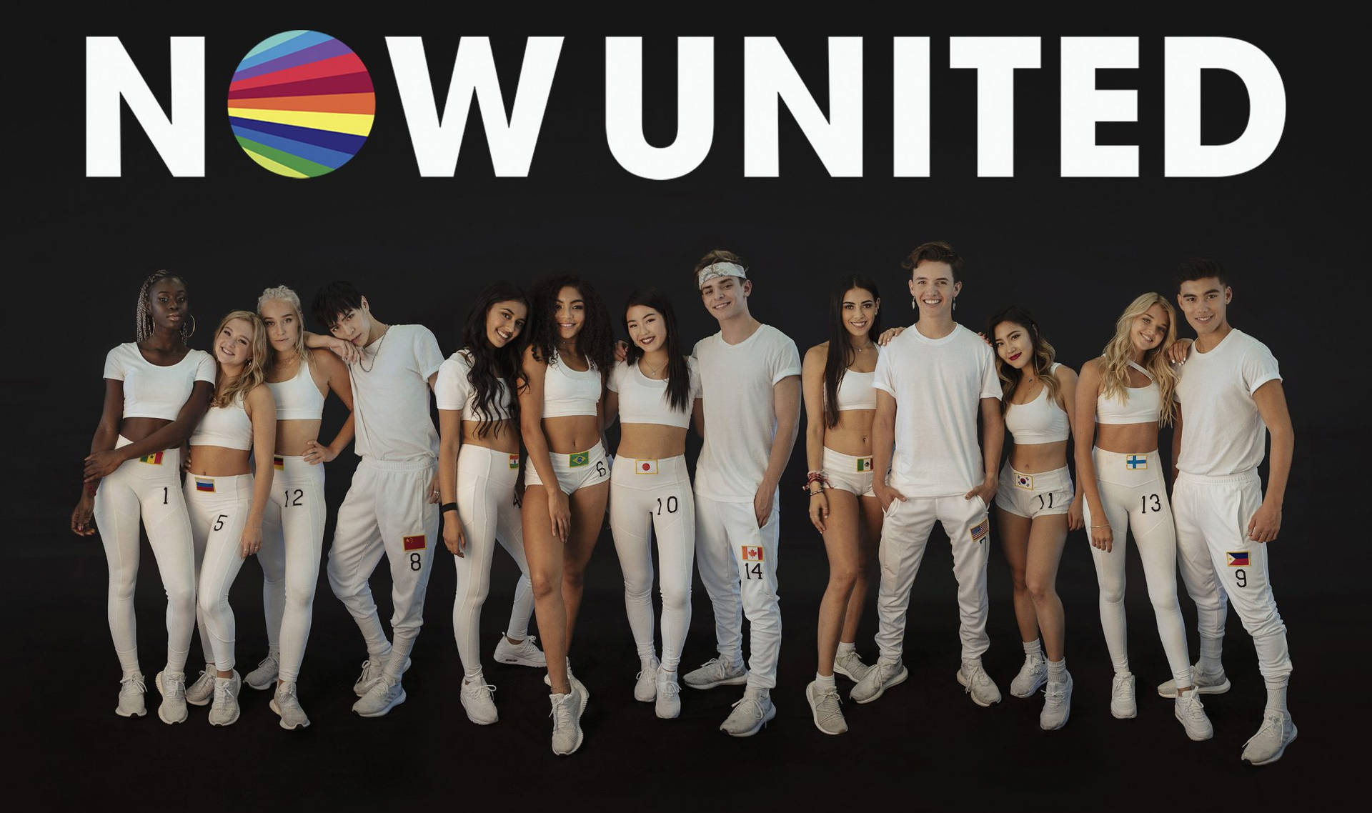 一群穿著白色運動服的年輕表演者為NOW UNITED標誌擺姿勢。