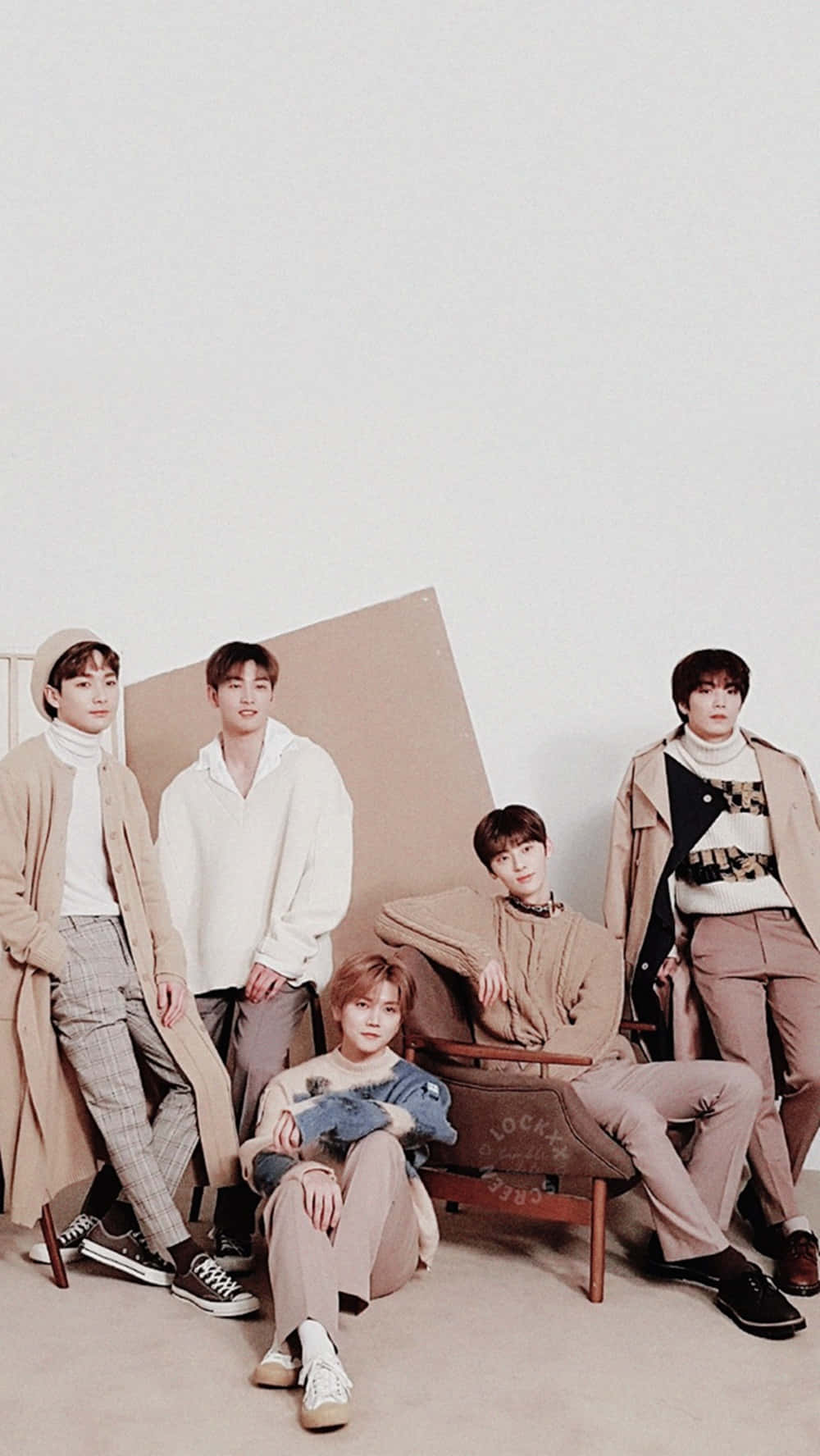 Nuest K-pop 男子團體中性服裝照 壁紙 — 五位時尚年輕男士在簡約風格的米色調工作室中隨意擺姿勢，光線柔和。