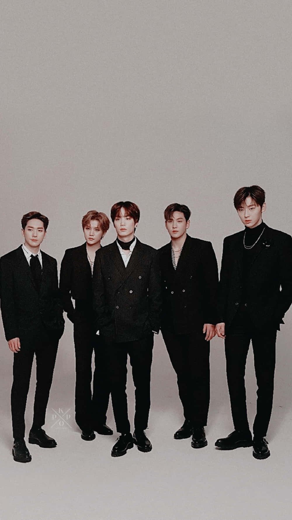 NUEST K-pop男子團體時尚西裝造型 壁紙 — 五位穿著黑色西裝的時尚男士在純灰色工作室背景前自信地擺姿勢。