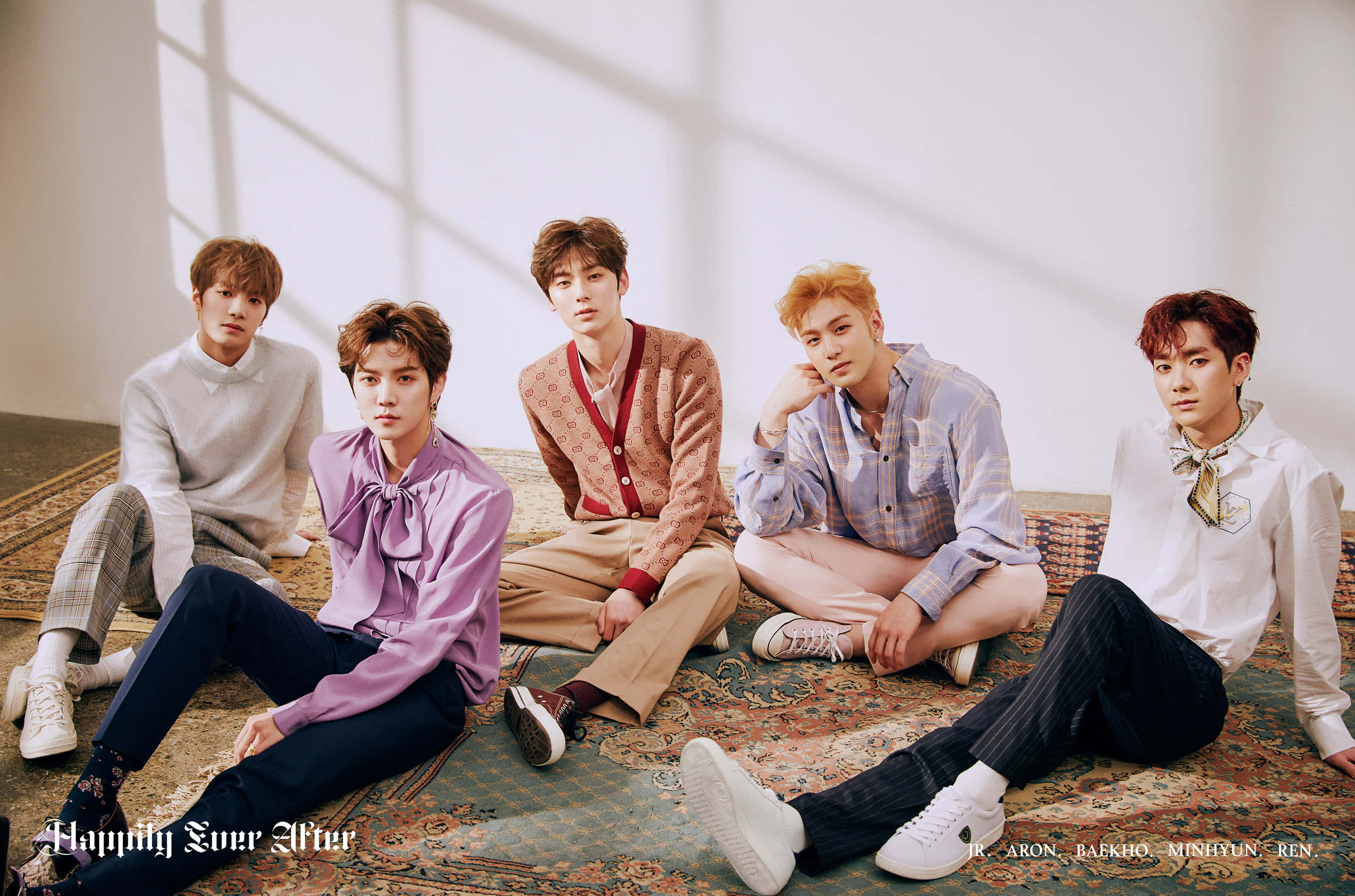 NUEST KPOP 男子團體休閒照 壁紙 — 五位時尚年輕男士在簡約工作室的明亮窗光下，隨意地擺姿勢在圖案地毯上。