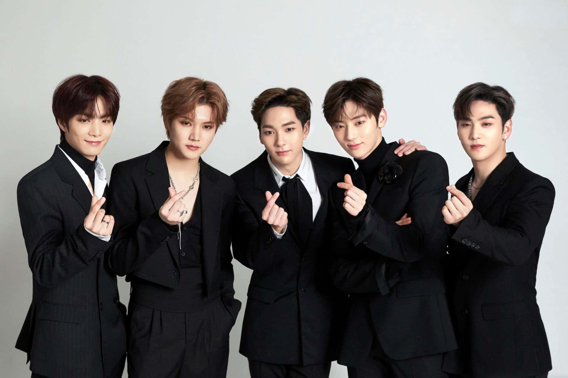 NUEST KPOP 男子團體西裝照 壁紙 — 五位穿著黑色西裝的時尚年輕男性在純白背景前自信地擺姿勢，手勢協調一致。