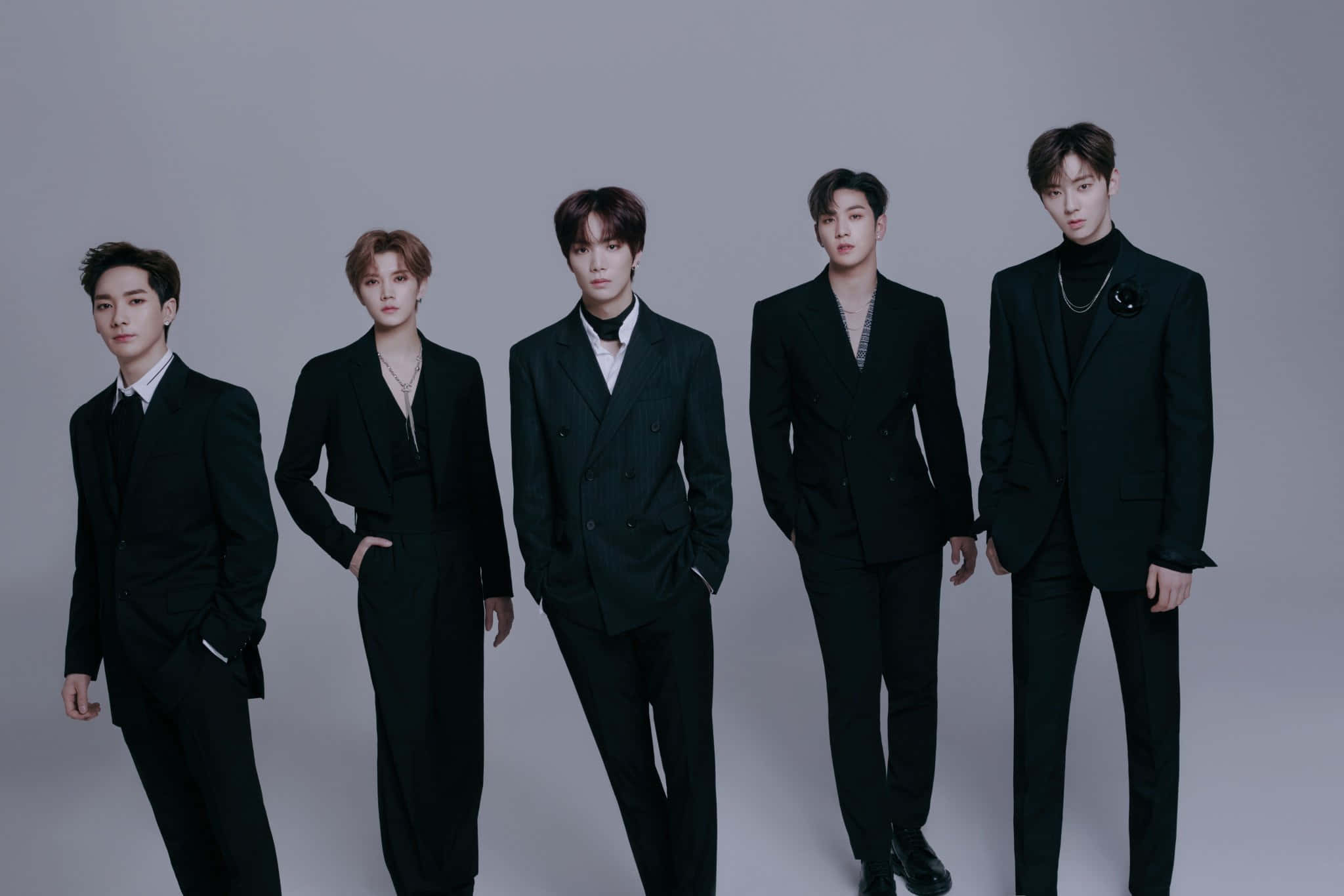 NUEST KPOP 男子團體酷感拍攝 壁紙 — 五位時尚年輕男士身穿俐落黑色西裝，在純灰色攝影棚背景前自信地擺姿勢。