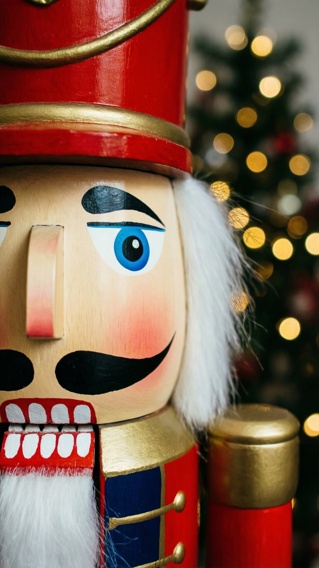 Nutcracker Face Close-Up 壁紙 — 傳統木製胡桃夾子士兵的 close-up，藍眼睛、白鬍子，背景是模糊的聖誕樹，掛著金色燈飾。