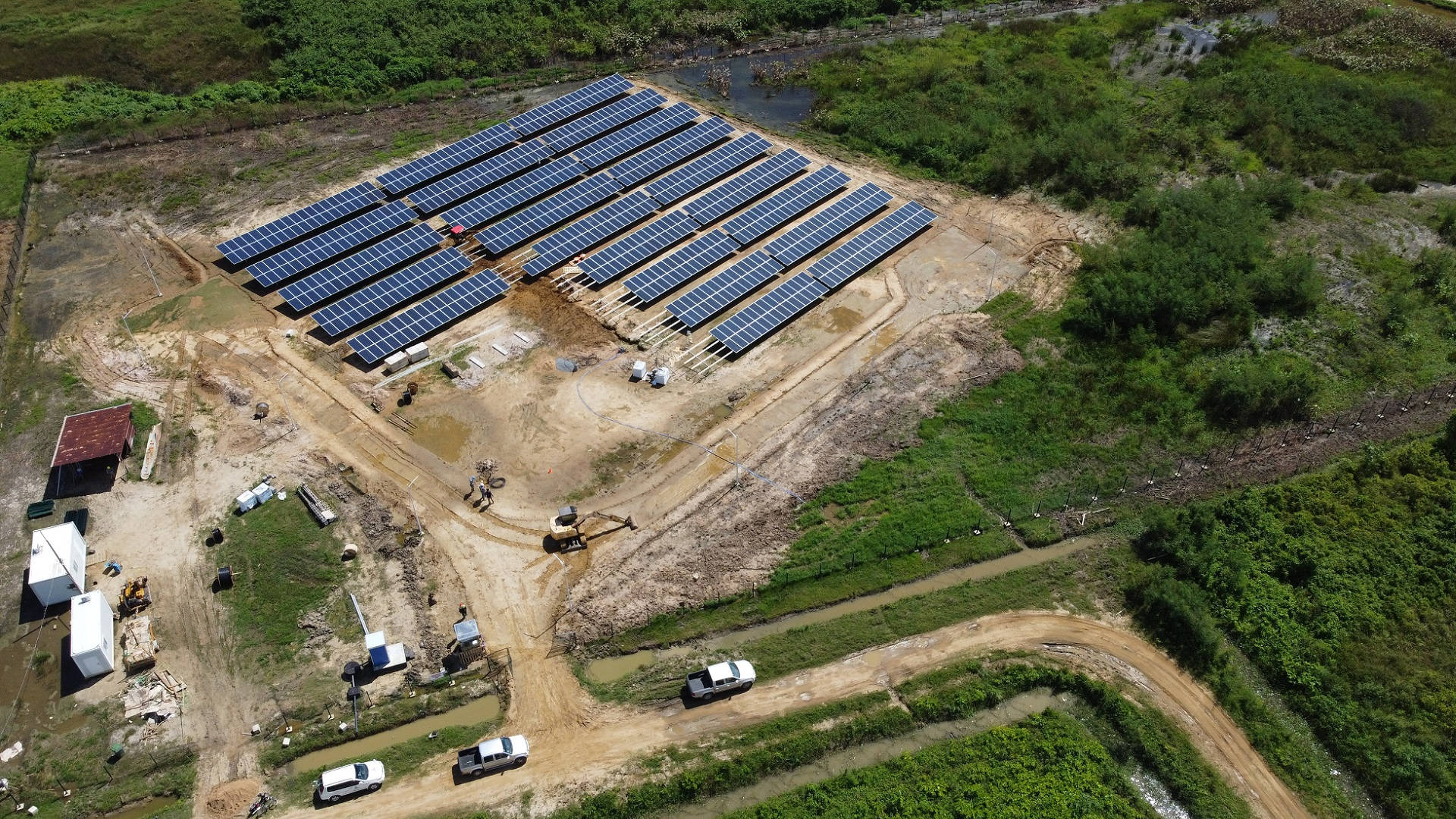 NV Energy 太陽能農場建設 壁紙 — 大型太陽能發電廠正在建設中的鳥瞰圖，周圍環繞著茂密的綠色植被和帶有車輛的泥路。