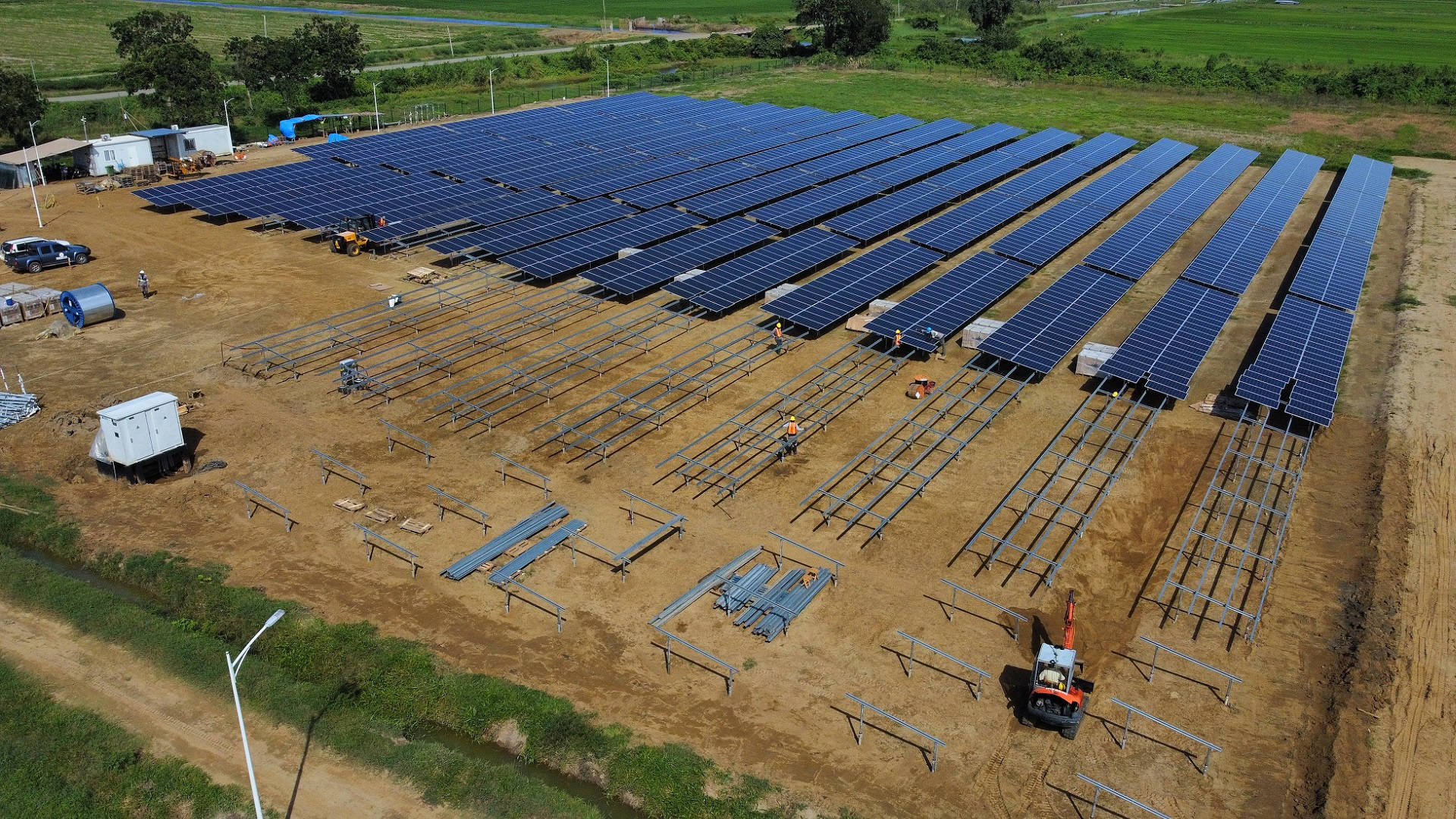 NV Energy 電力系統安裝 壁紙 — 從空中俯瞰一個正在建設中的太陽能農場，工人和機械在一個被綠色田野包圍的泥土地上工作。