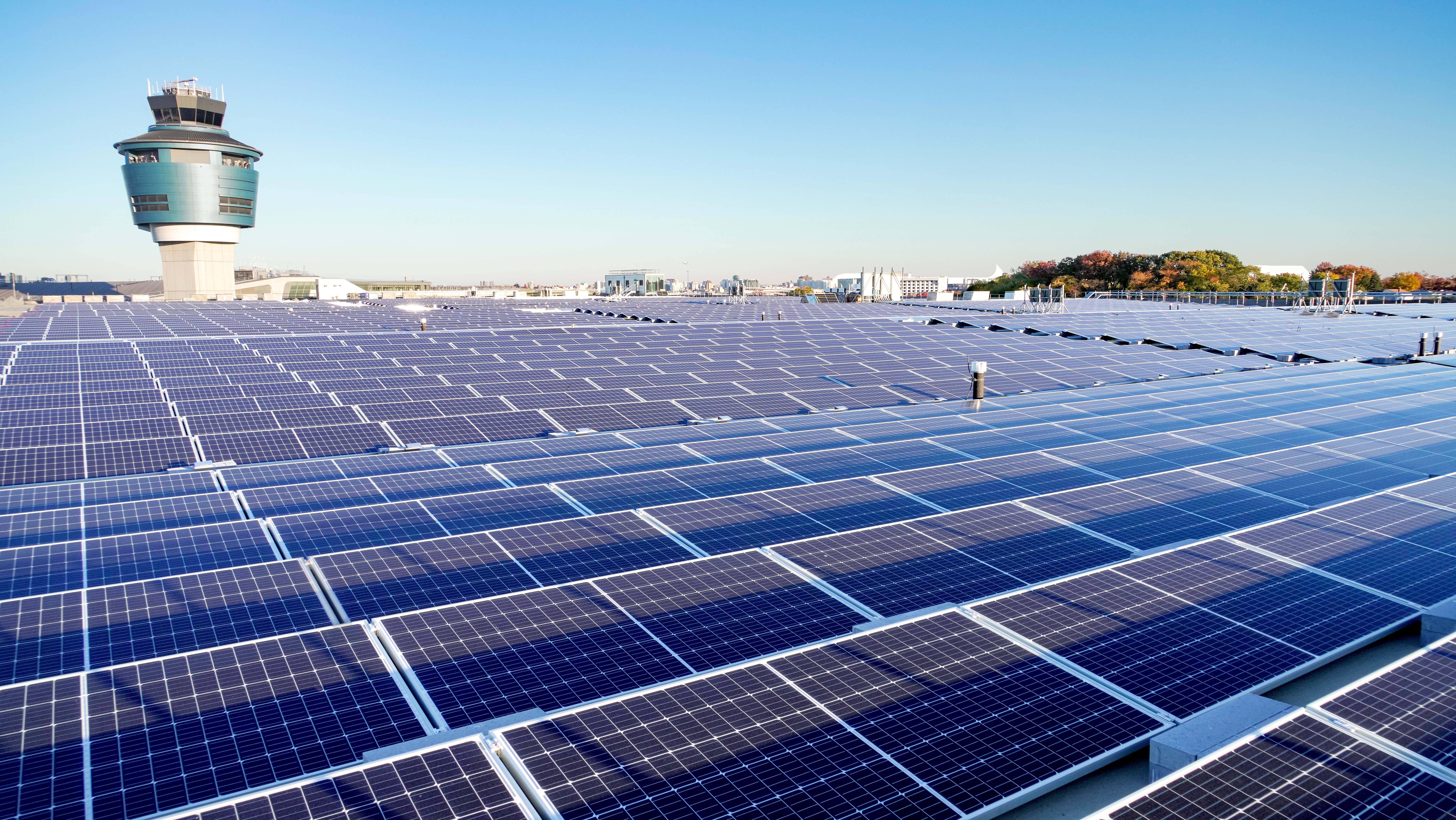 NV Energy光伏電力站 壁紙 — 一排排藍色太陽能板在晴朗的藍天下延伸至屋頂，遠處有機場控制塔。