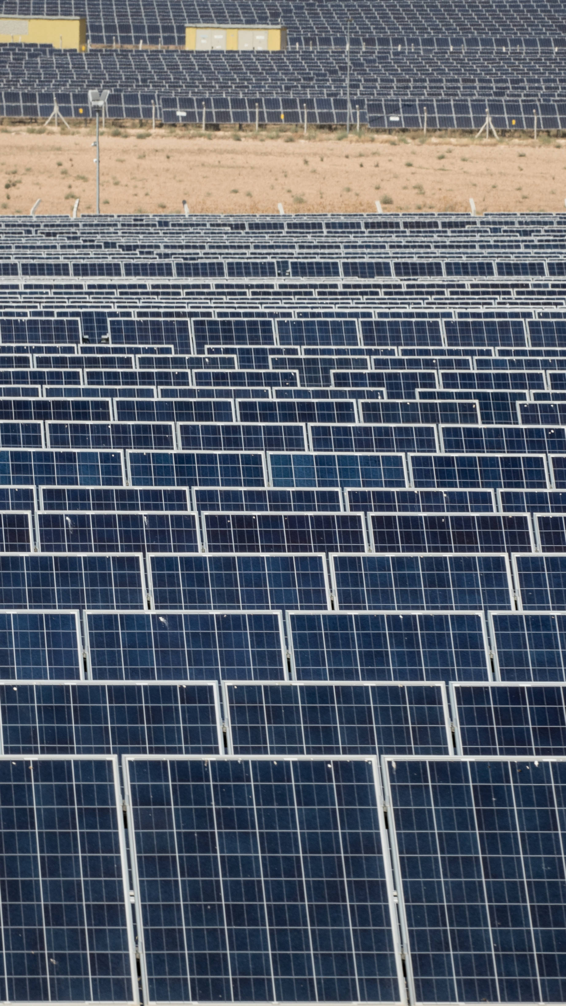NV Energy太陽能農場 壁紙 — 一排排深藍色太陽能板在明亮的日光下延伸在乾燥的沙漠景觀中。