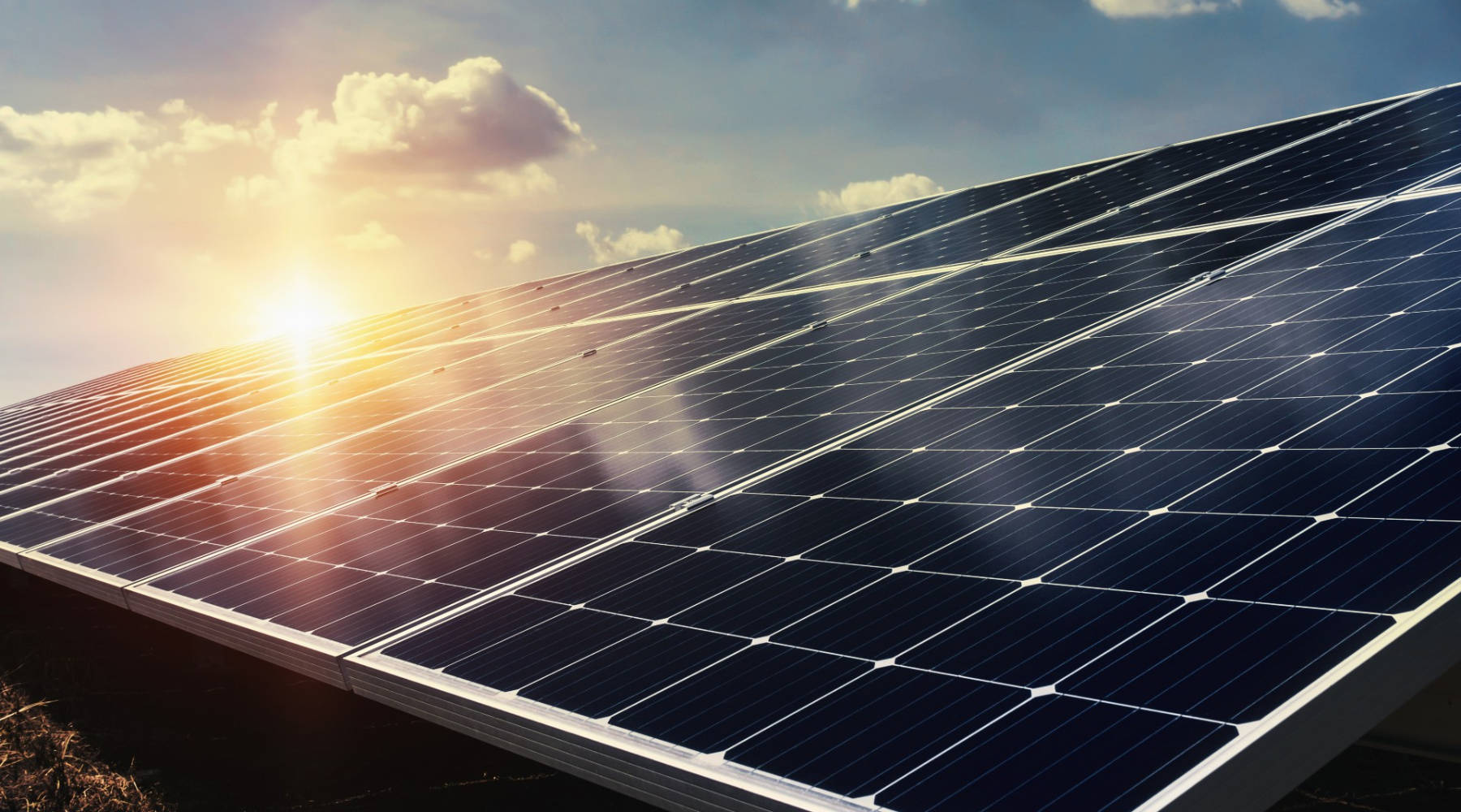 NV Energy日出攝影 壁紙 — 一排排太陽能板在金色日出下閃閃發光，在晴朗的藍天和散落的雲朵上投下長長的影子。