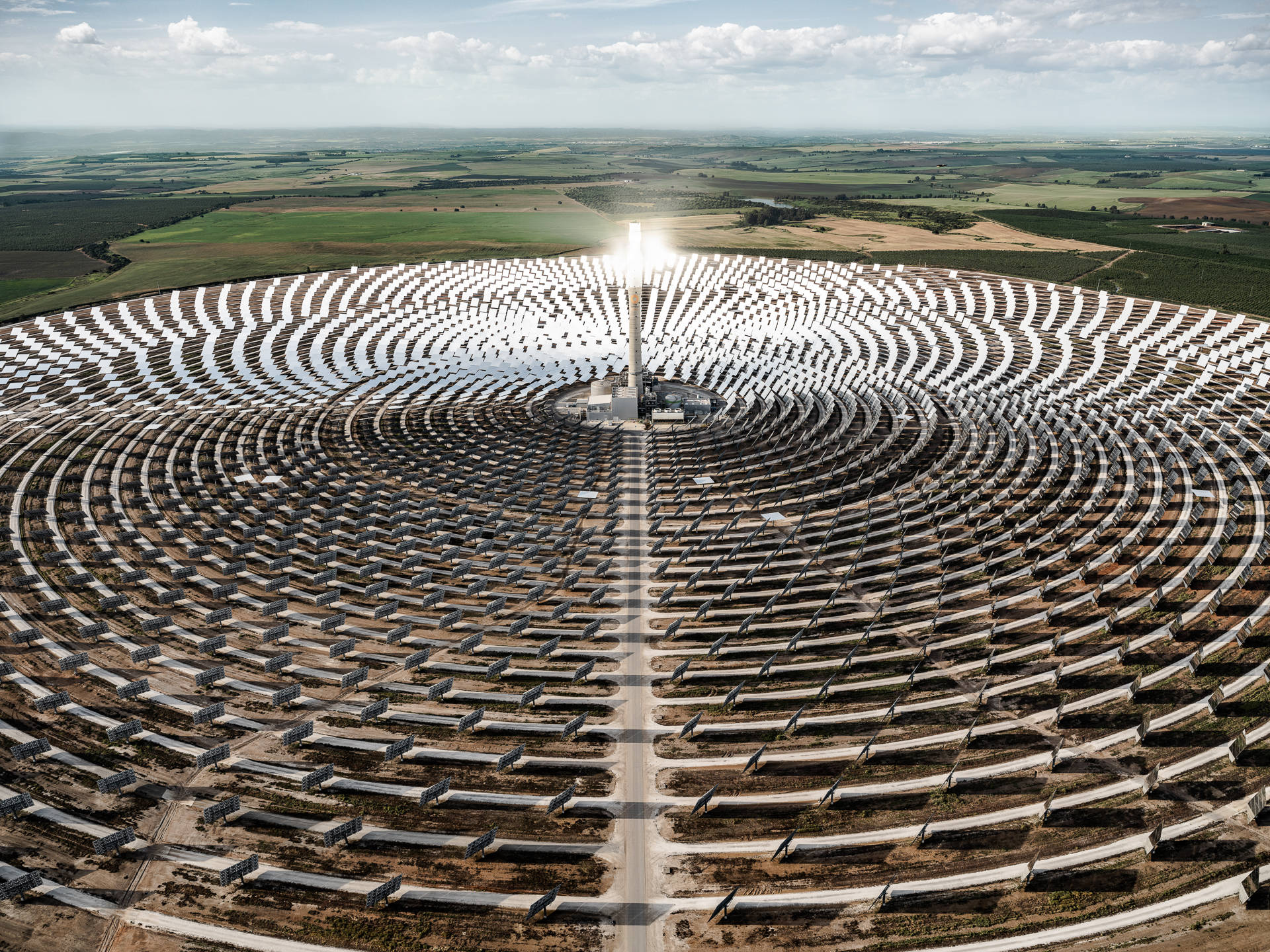 NV Energy環形太陽能板系統 壁紙 — 從空中俯瞰一個巨大的太陽能發電廠，數千面鏡子在部分多雲的天空下向外輻射向中央塔。