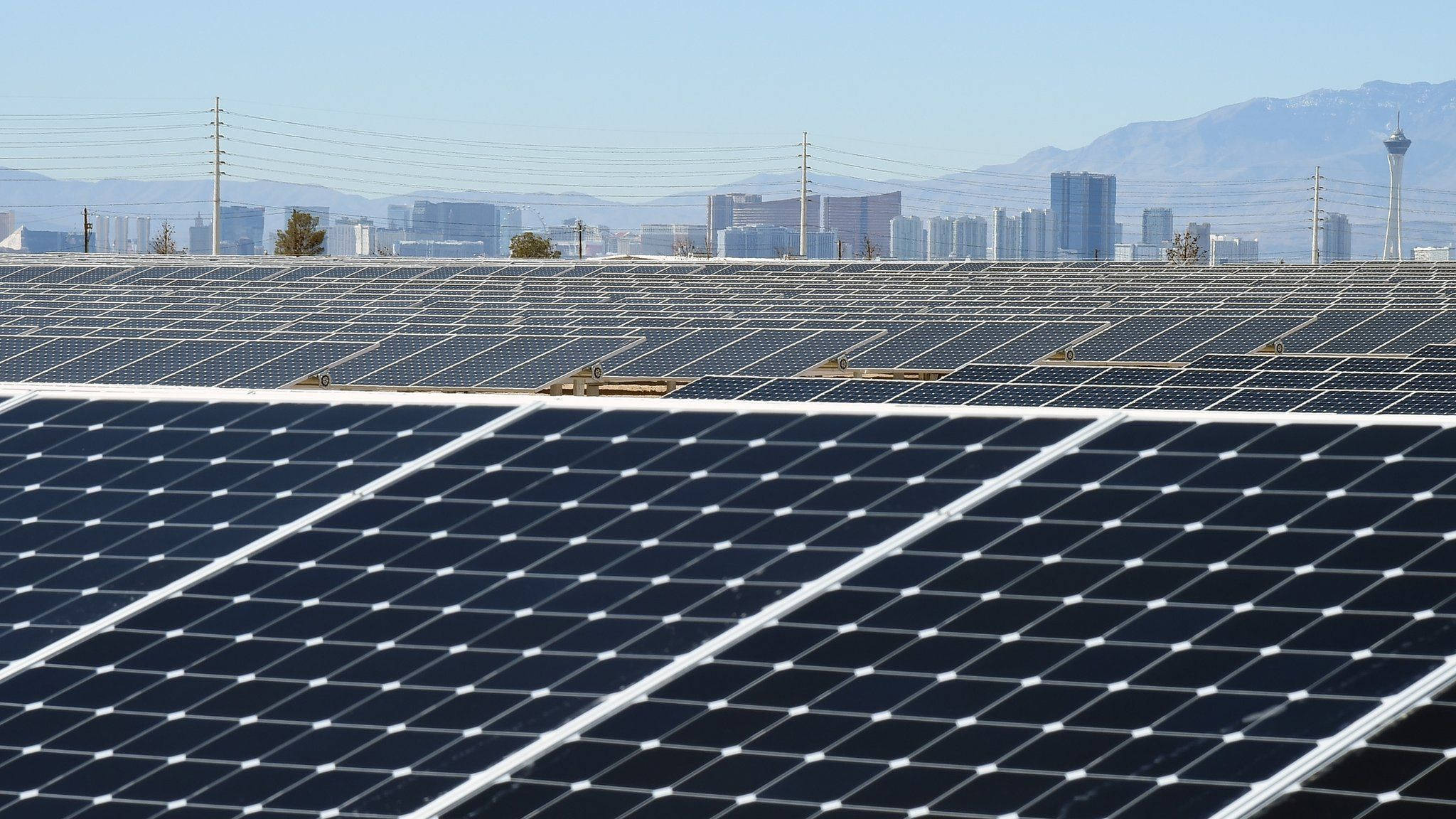由NV能源電廠供電的城市 壁紙 — 一排排太陽能板延伸穿過沙漠景觀，遠處有城市天際線和山脈，在清澈的藍天下。