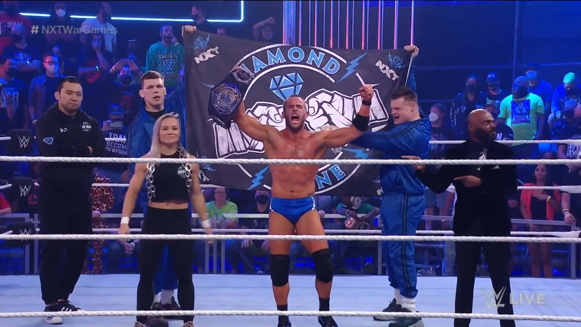 NXT輕量級冠軍Roderick Strong 壁紙 — 一位穿著藍色短褲的勝利WWE摔角手在擂台上高舉冠軍旗幟慶祝勝利，周圍粉絲歡呼。