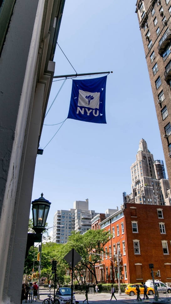 NYU旗幟懸掛在繁忙城市街道的建築物之間，有行人和黃色的士。