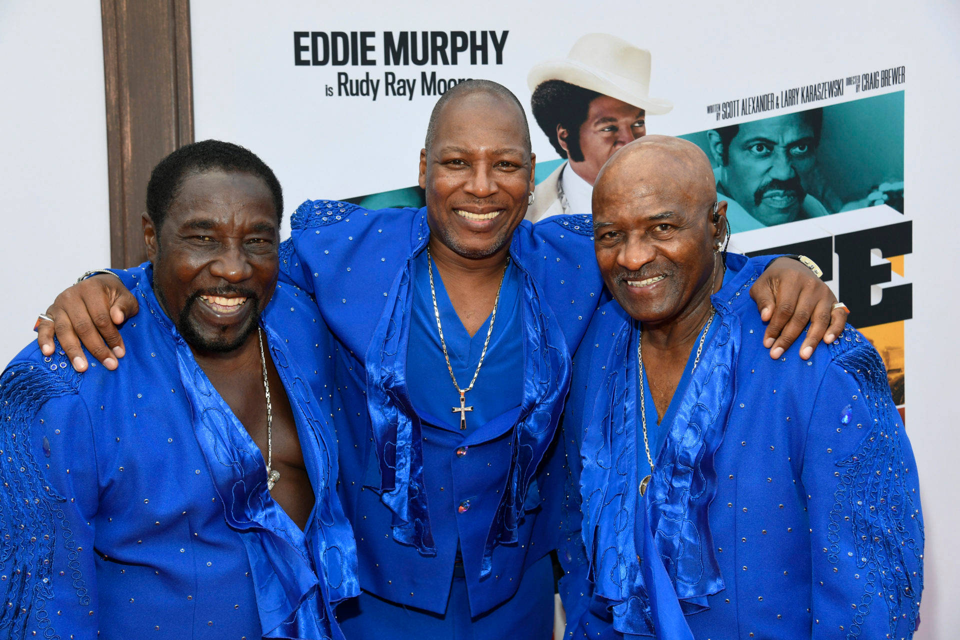 O'Jays 舞台演出 壁紙 — 三位身穿閃亮藍色亮片服裝的男士在電影首映禮上對著鏡頭溫暖微笑。