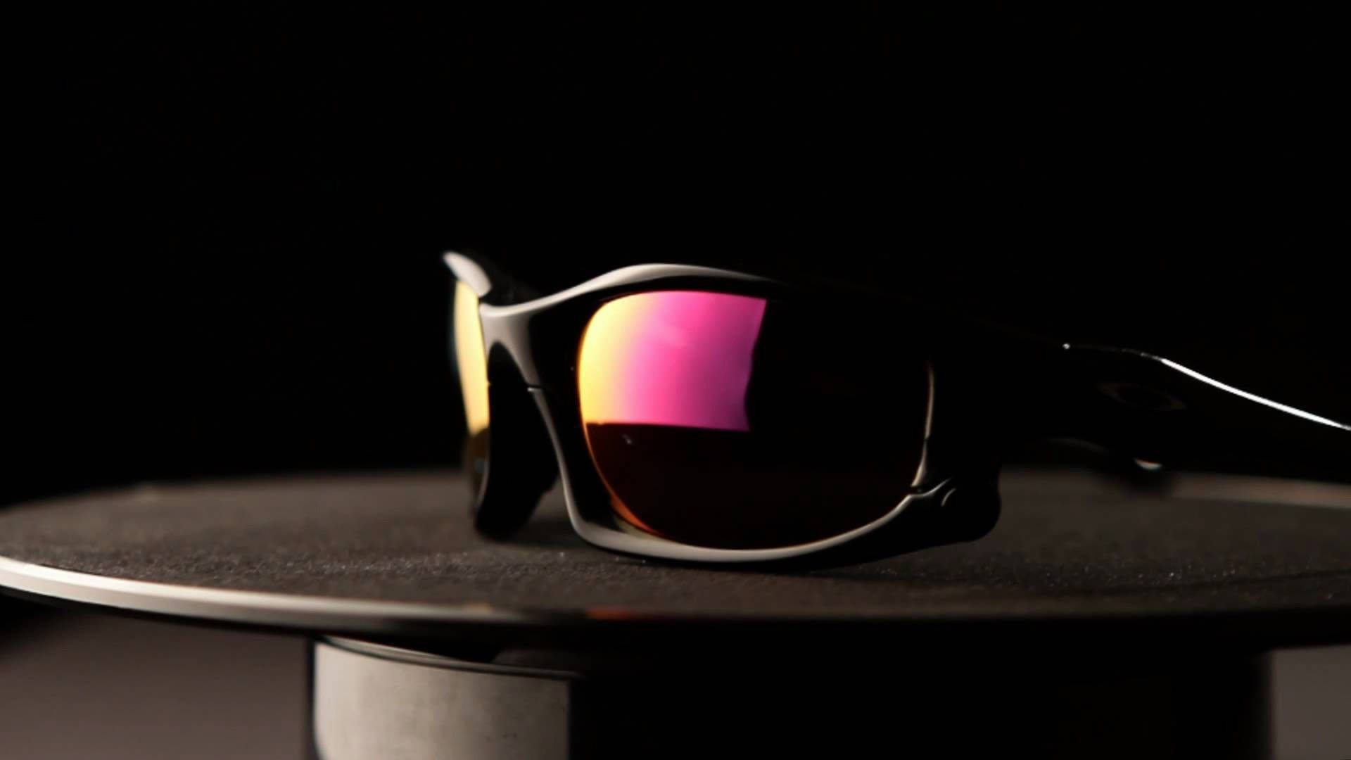 Oakley Holbrook 偏光太陽眼鏡 Midnight Sun 壁紙 — 一副時尚的黑色太陽眼鏡，帶有虹彩粉紅色和金色鏡片，放置在黑色背景的深色紋理底座上。