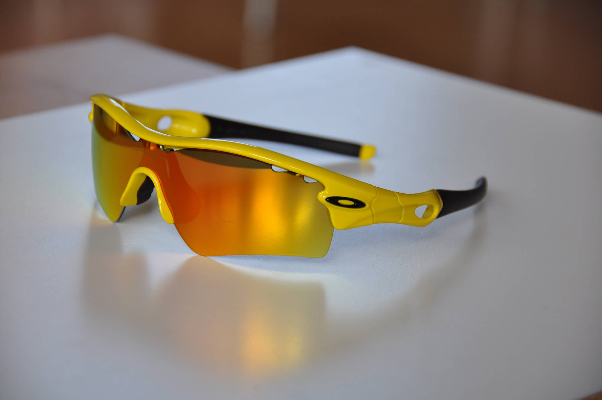 Oakley Radar 運動自行車太陽眼鏡 壁紙 — 鮮豔黃色運動太陽眼鏡，配備反光橙色鏡片，放置在潔白表面上。