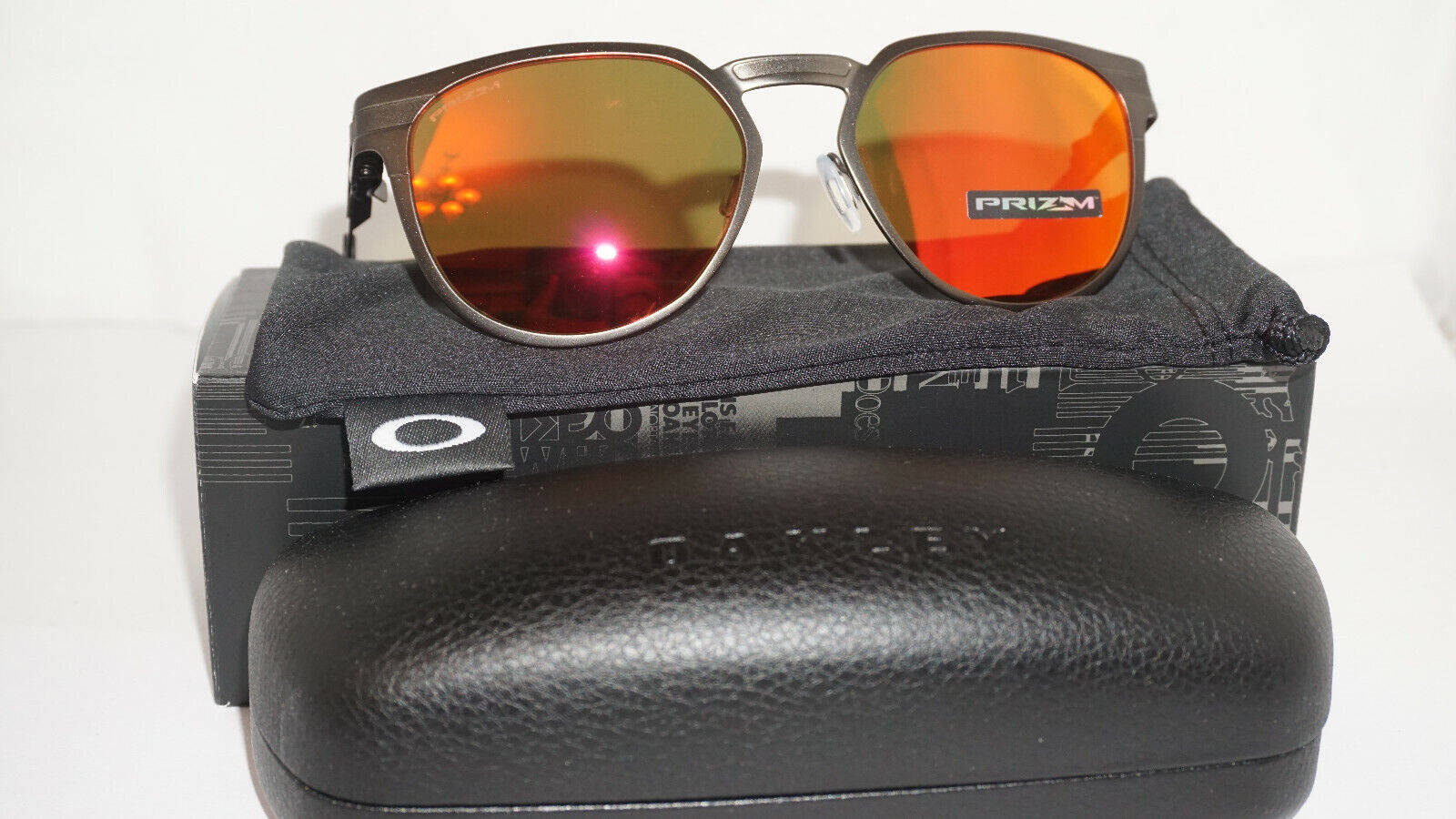 Oakley 太陽眼鏡與鏡片收納盒 壁紙 — 一副帶有鮮豔橙色鏡面鏡片的Oakley太陽眼鏡，放在其品牌眼鏡盒和眼鏡布上，背景為純白色。
