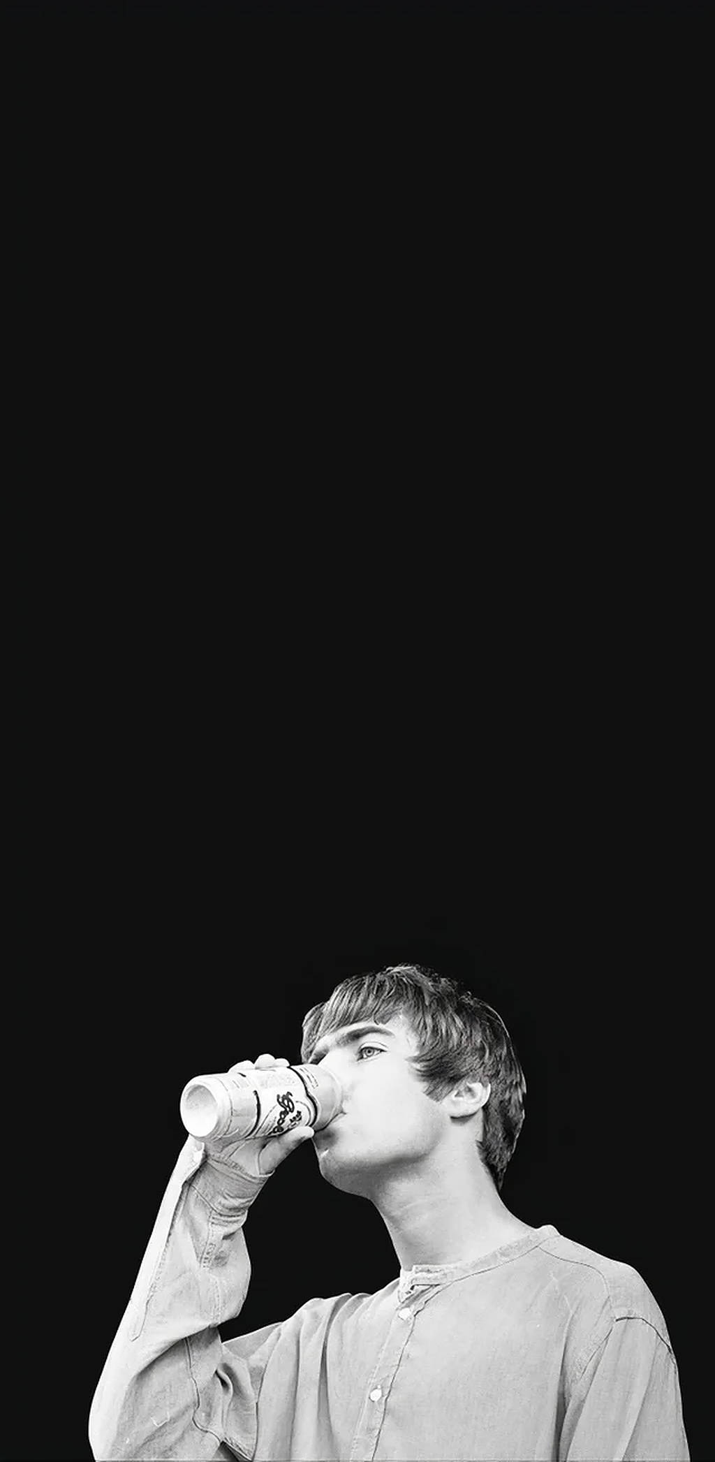 Oasis樂隊Liam Gallagher 壁紙 — 一個黑白年輕男子在黑色背景前用紙杯喝水。