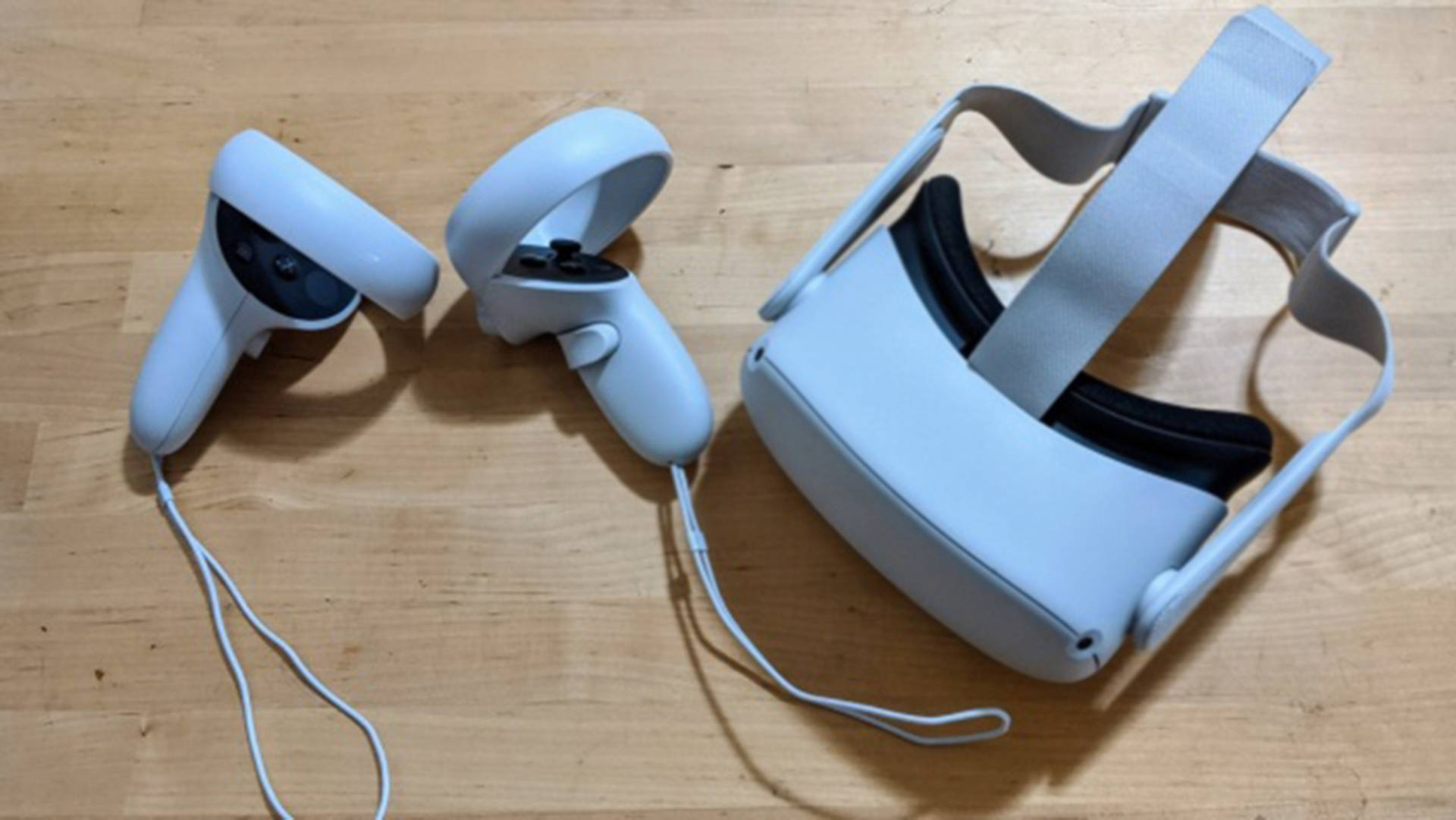 天空藍色Oculus Quest 2 壁紙 — 淺灰色VR頭戴式裝置和控制器放在溫暖的木地板上，光線柔和自然。