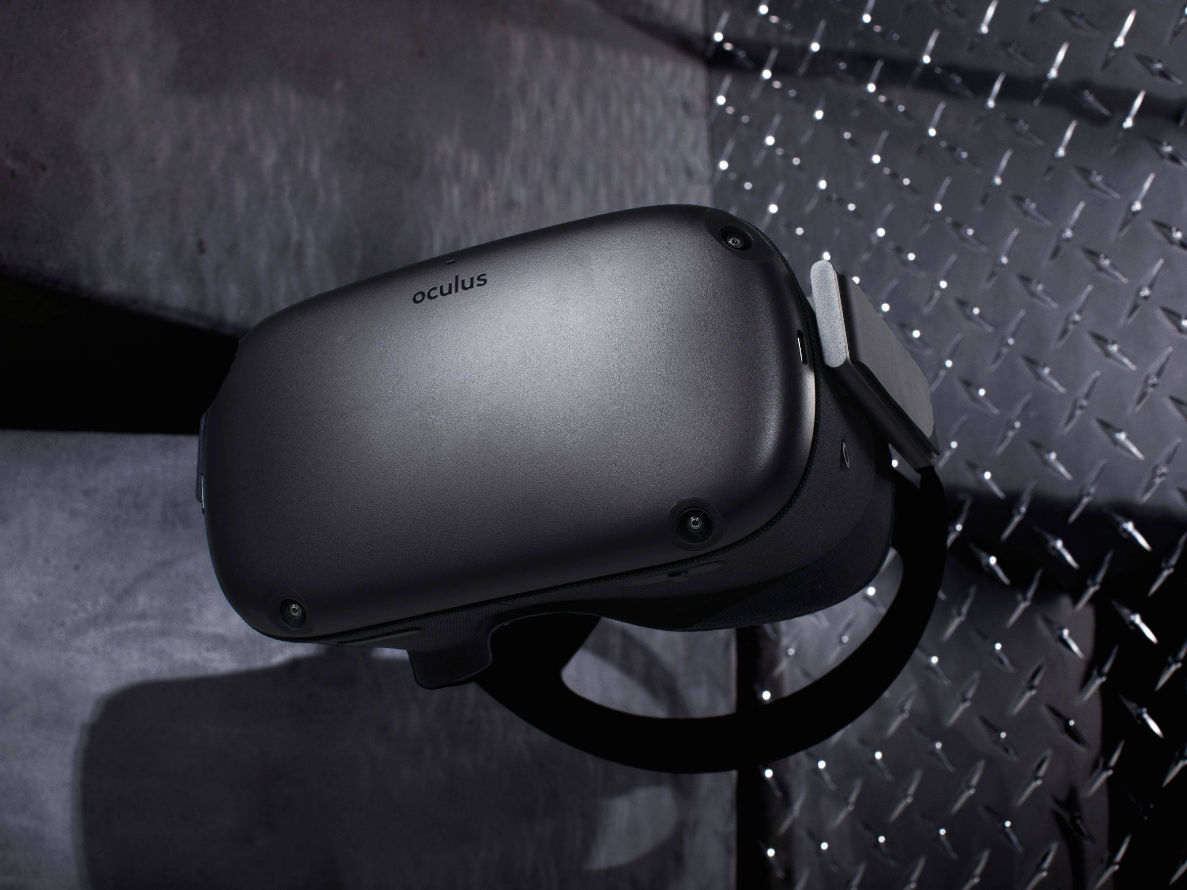 Oculus Quest 2金屬背景 壁紙 — 一個時尚的黑色Oculus VR頭戴式裝置放置在紋理金屬表面上，在戲劇性的工作室燈光下。