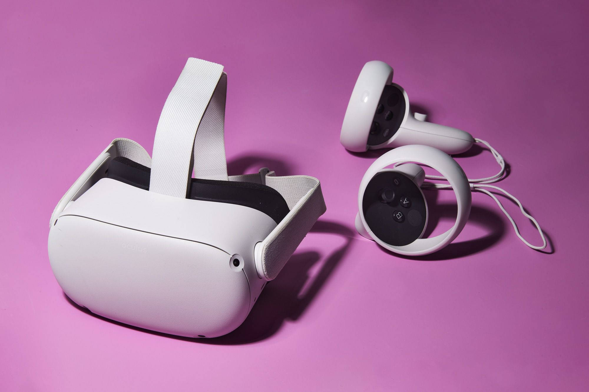粉紅背景 Oculus Quest 2 壁紙 — 白色VR頭戴式裝置和控制器放置在充滿活力的粉紅色表面上，投射出柔和的陰影。
