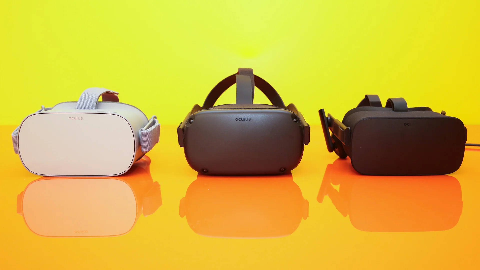 Oculus Quest 2 VR裝置 壁紙 — 三個白色、灰色和黑色的 Oculus VR 頭戴式裝置放在光滑的橙色表面上，背景為明亮的黃色。