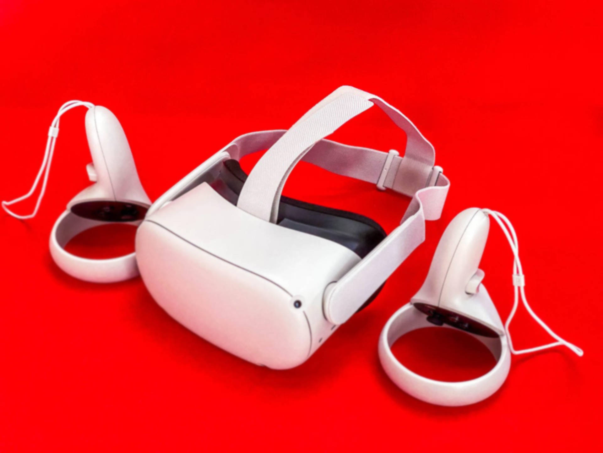 Oculus Quest 2紅色背景 壁紙 — 一個時尚的白色VR頭戴式裝置和控制器放置在鮮明的紅色背景上，展示現代沉浸式技術。