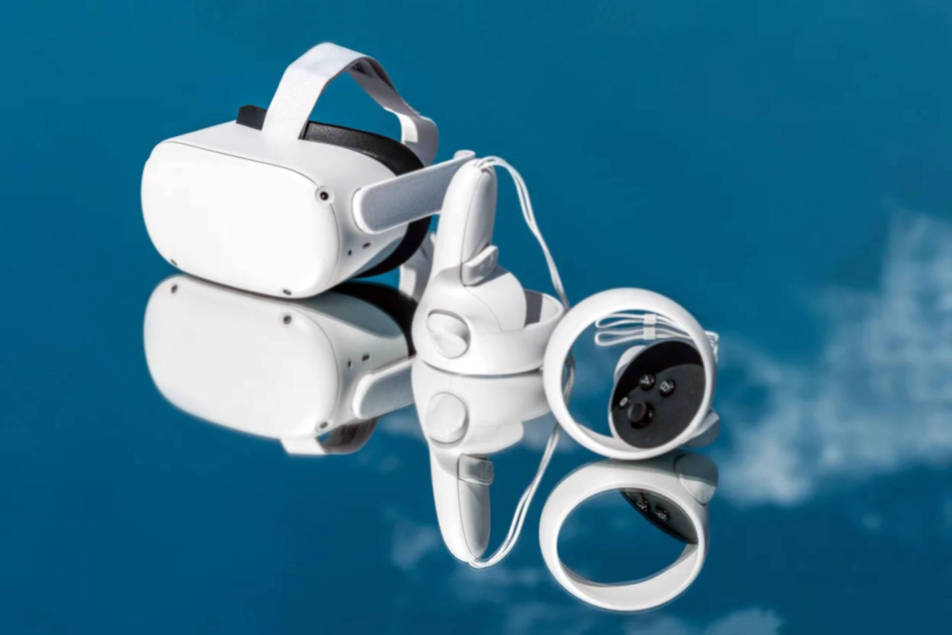 Oculus Quest 2 藍色背景 壁紙 — 白色VR頭戴式裝置和控制器放在反射藍色表面上，映照出多雲的天空。