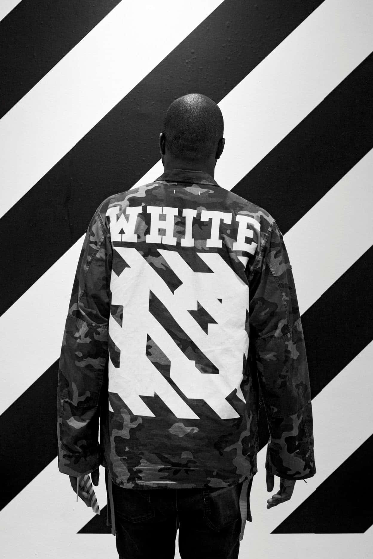 單色濾鏡 Off White iPhone 壁紙 — 一個人背對鏡頭站立，身穿迷彩外套，上面有粗體白色「WHITE」文字和圖案，背景是黑白對角條紋牆。