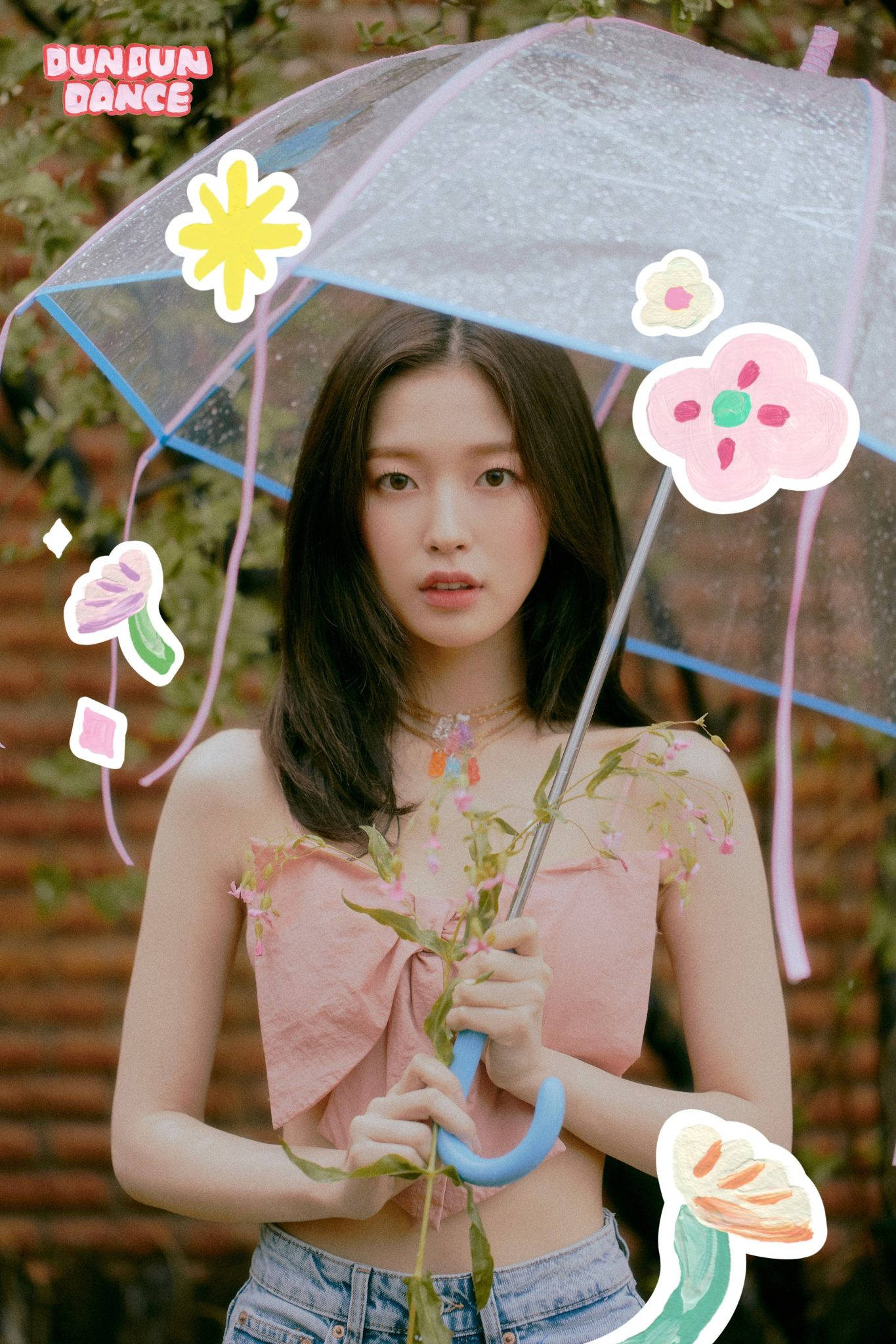 Oh My Girl Arin 持透明雨傘 壁紙 — 一位年輕女性在磚牆背景下拿著一把帶有卡通花朵的透明雨傘。