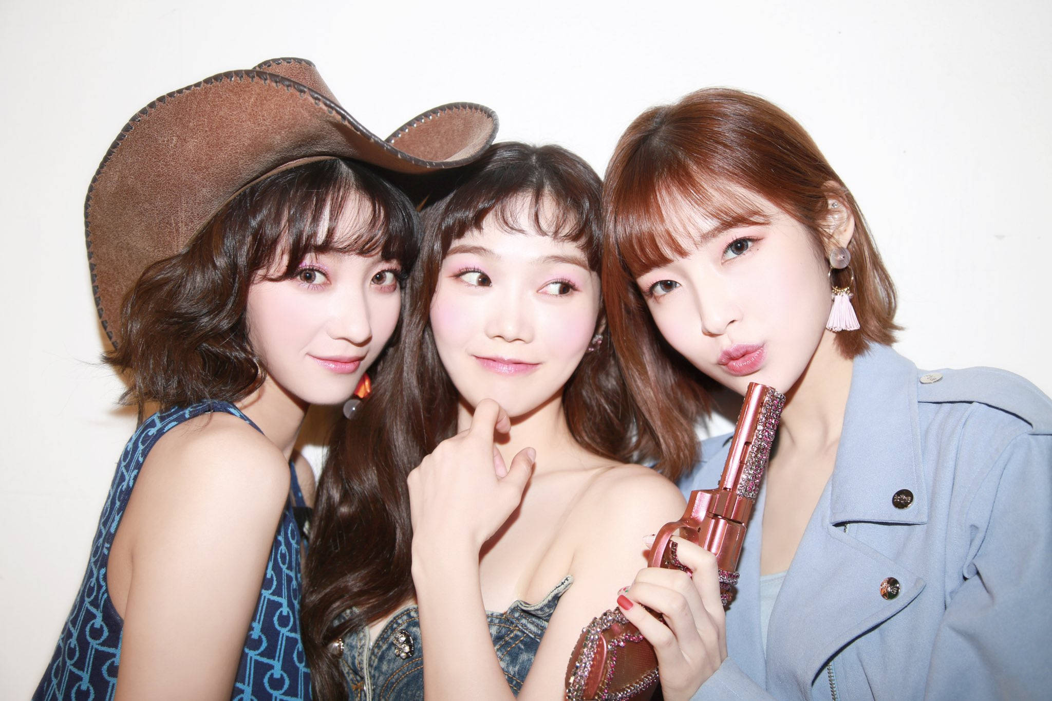 Oh My Girl Banhana Binnie、Hyojung 與 Arin 奶牛女郎造型 壁紙 — 三位時尚年輕女性在純白背景前俏皮擺姿勢，一人戴著牛仔帽，另一人拿著閃亮玩具槍。