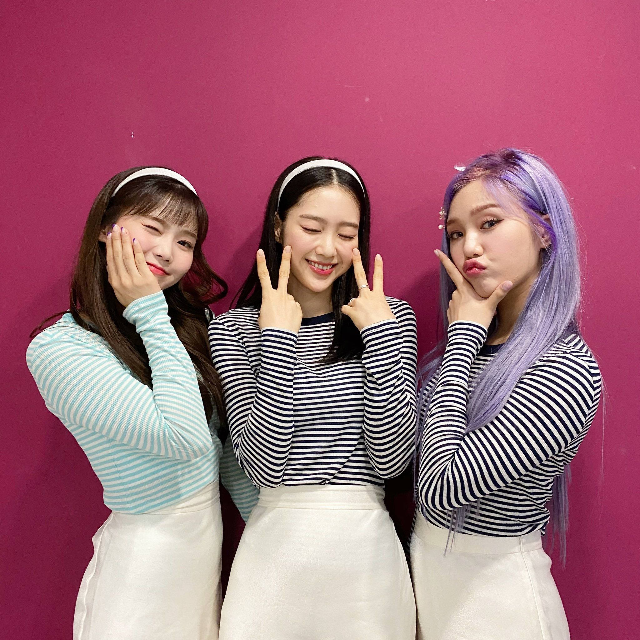 OH MY GIRL Hyojung、Jiho 與 Mimi 壁紙 — 三位微笑的年輕女性在充滿活力的粉紅色牆前頑皮地擺姿勢，做出和平手勢和搞笑表情。