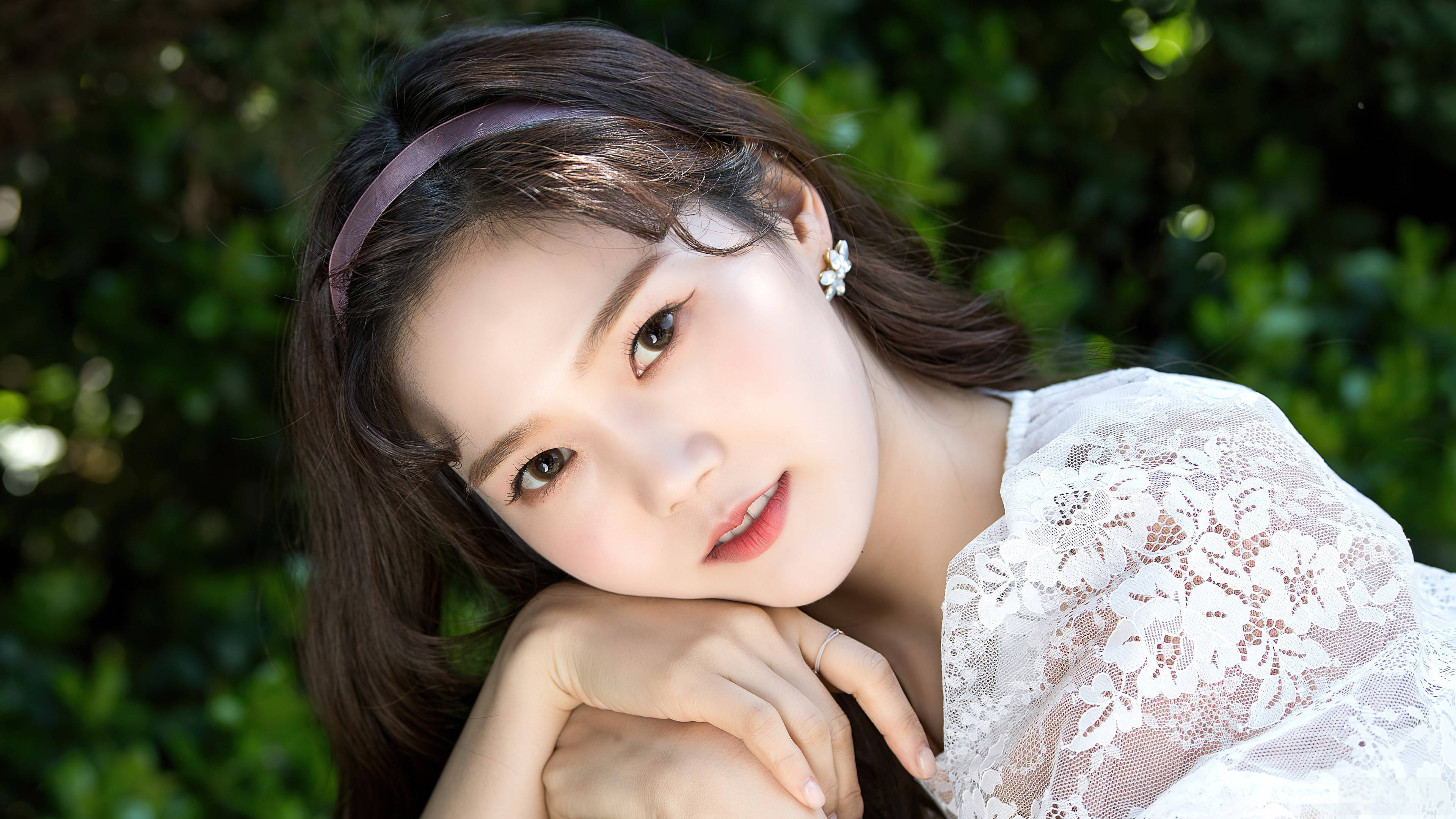 Oh My Girl Hyojung 深邃凝視 壁紙 — 一位深色頭髮、戴著紫色頭帶的年輕女子，雙手托腮，在茂密的綠色樹葉背景下溫柔地凝視著鏡頭。