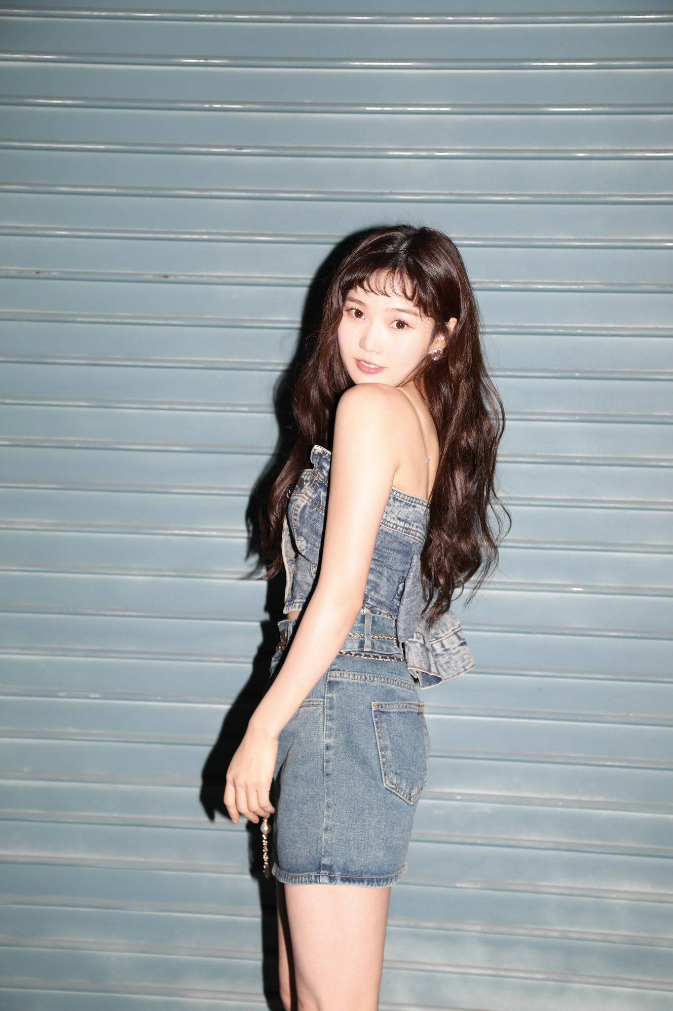 Oh My Girl 主唱 Hyojung 舞台光芒四射 壁紙 — 一位身穿牛仔裙的年輕女性，在灰色金屬快門背景前，帶著俏皮的眼神擺姿勢。
