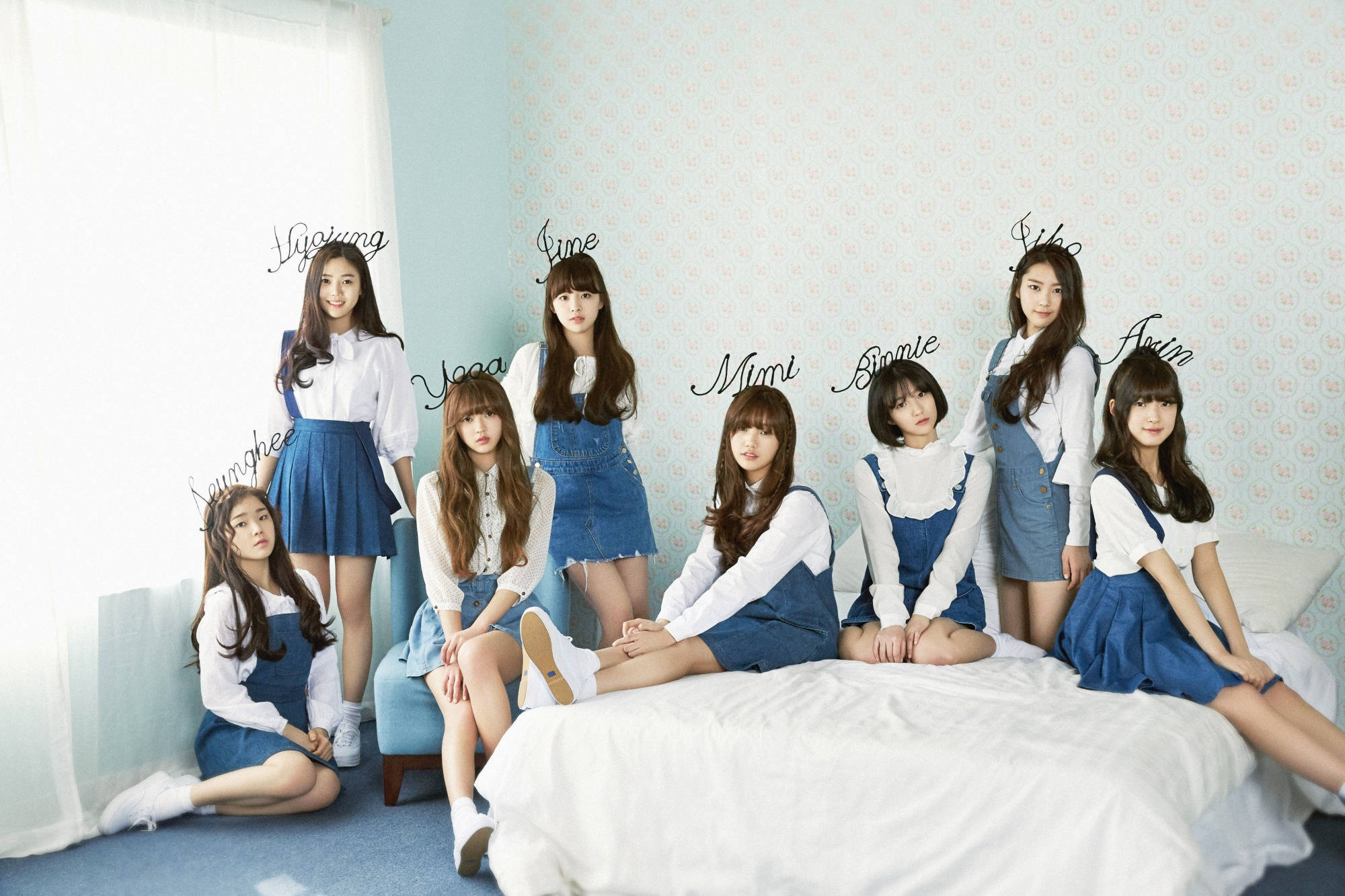 Oh My Girl 名字頭帶造型 壁紙 — 七位年輕女性身穿白色襯衫和藍色連身褲，在柔和光線的房間裡，在帶有圖案壁紙的床和椅子上擺姿勢。