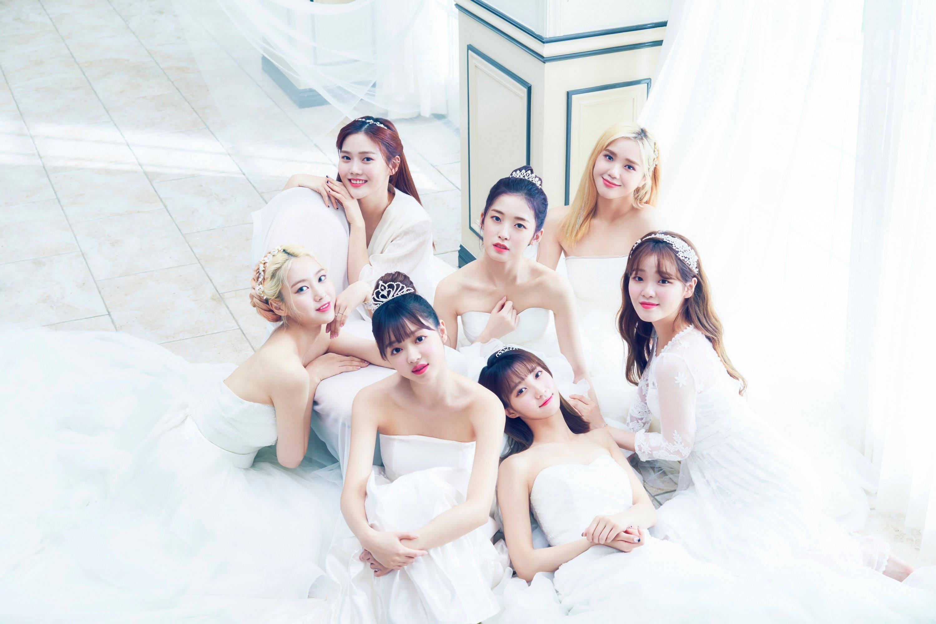 Oh My Girl 穿純白禮服的夢幻畫面 壁紙 — 七位年輕女性身穿優雅白色禮服和頭飾，在柔和自然光下於瓷磚地板上一起擺姿勢。